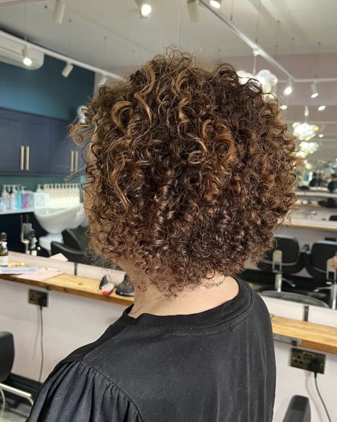 Back view of a person with short, tight, curly hair in an indoor hair salon.