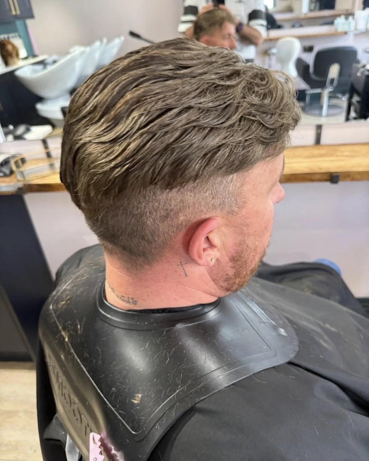 A man with a freshly cut hairstyle featuring a faded undercut and longer textured top, sitting in a salon chair.
