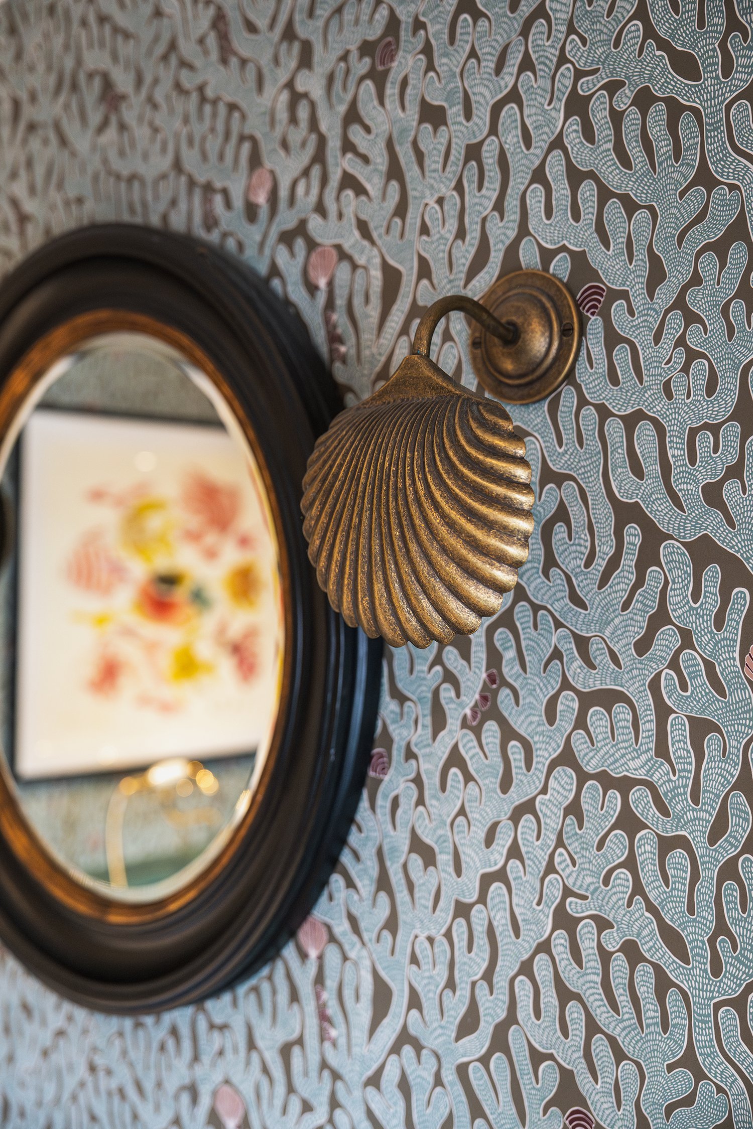 Vintage shell wall light against textured botanical wallpaper beside an antique mirror in a richly layered townhouse bathroom interior.