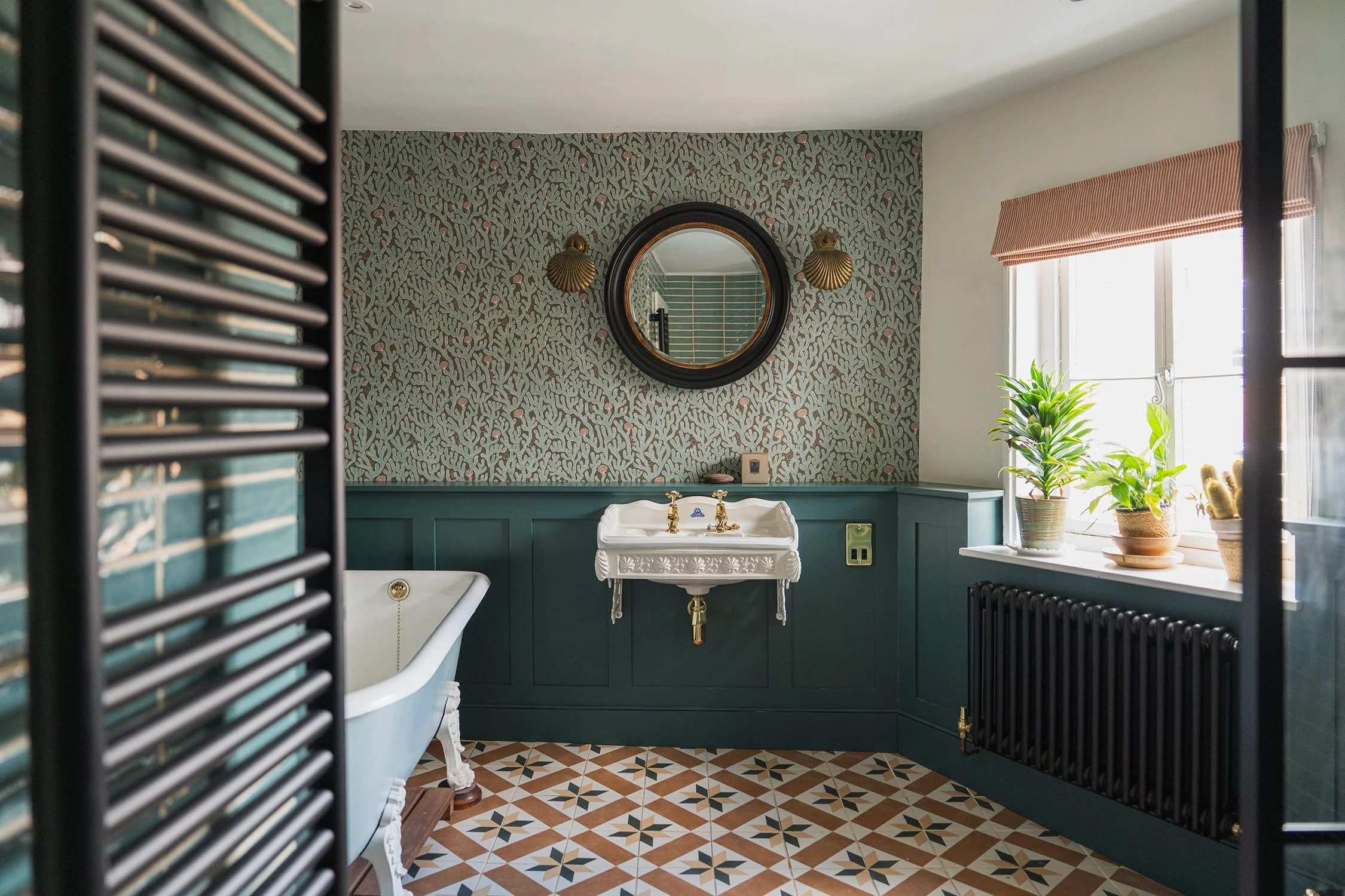 Elegant townhouse bathroom with statement wallpaper, decorative mirror, pedestal sink, and freestanding bath in a timeless period-inspired setting.
