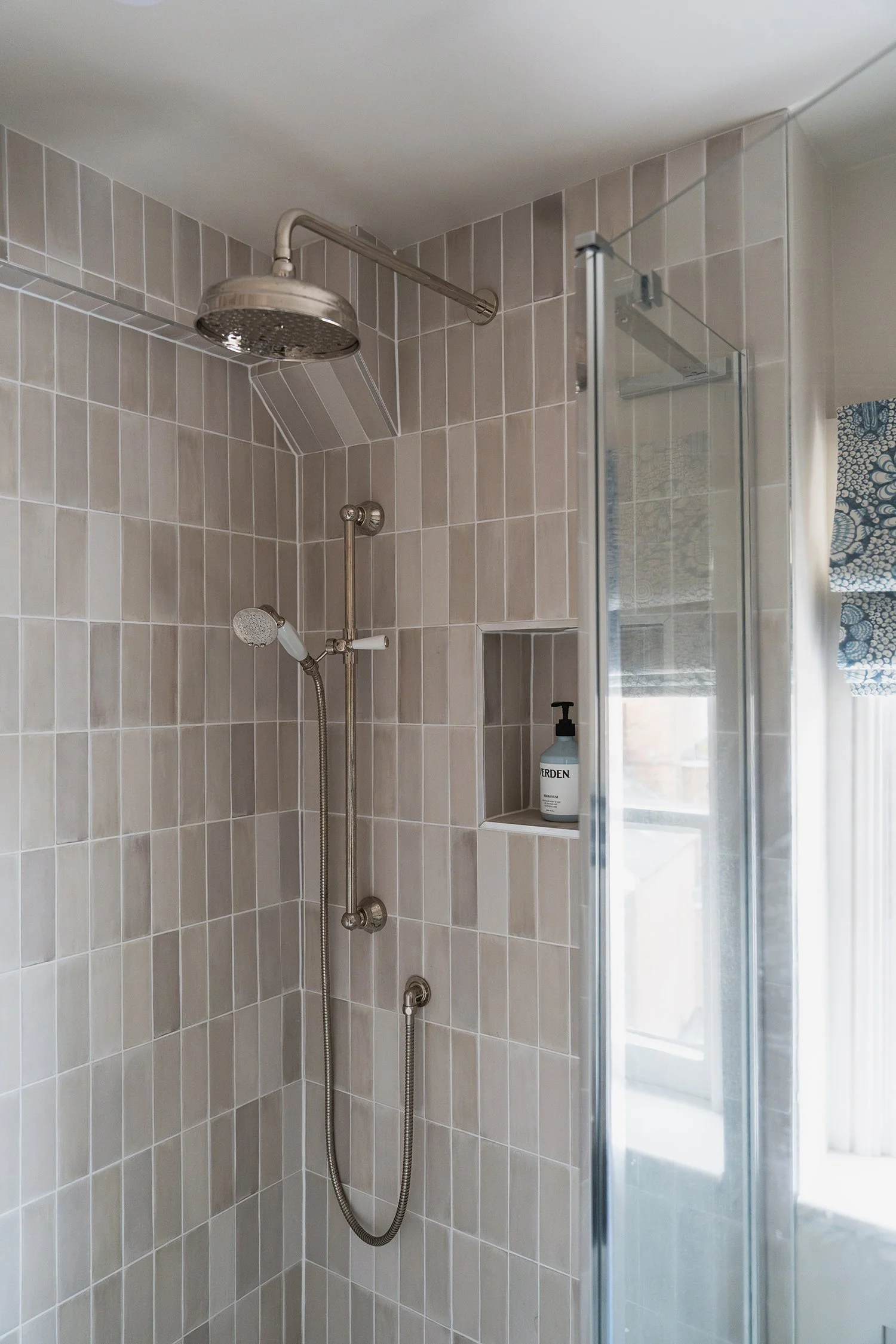 Walk-in shower with soft neutral wall tiles, vintage-style shower fittings, and natural light in an elegant townhouse bathroom.