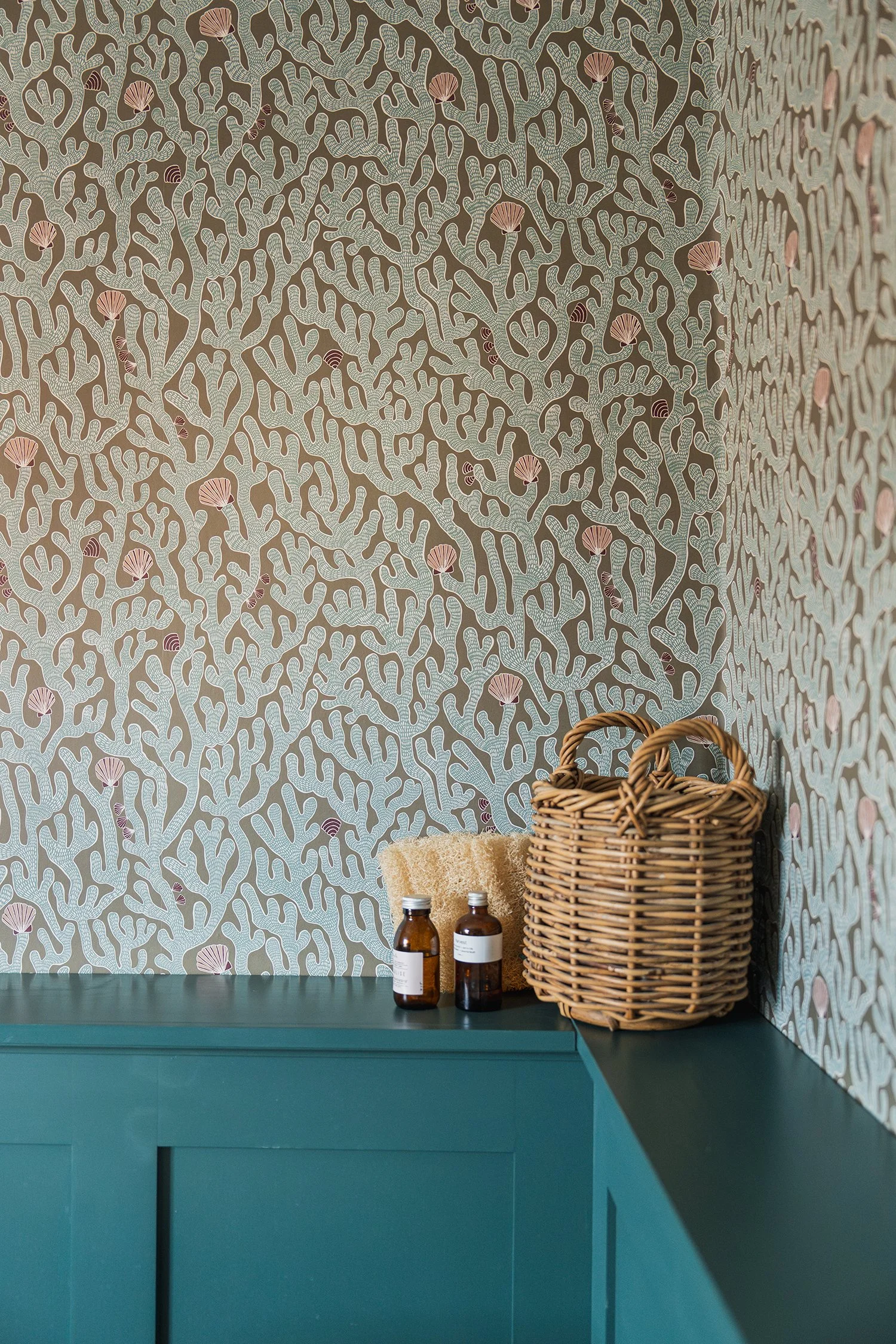 Textured botanical wallpaper and styled bathroom shelving detail with woven storage and artisan accessories in a warm townhouse interior.