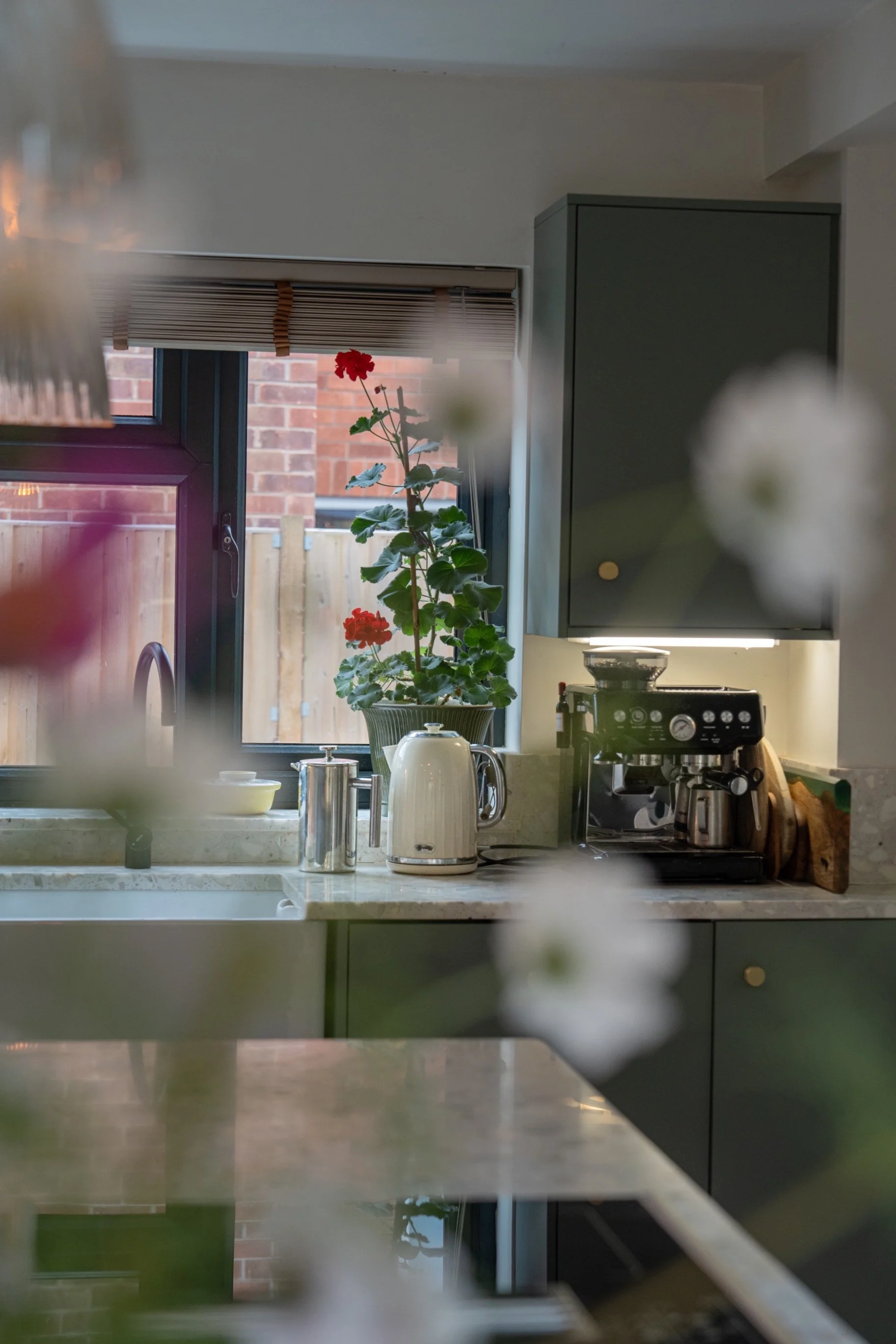 Contemporary kitchen interior with dark cabinetry, brass fixtures, coffee station, and natural light creating a warm modern home aesthetic.