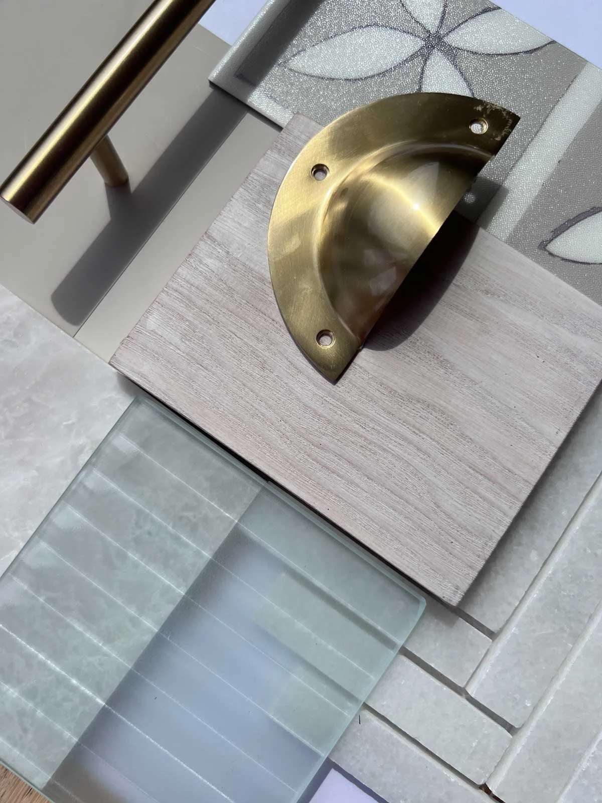 Close-up view of a brass sink basin mounted on a wooden countertop, with a decorative wall tile pattern in the background and a glass surface with striped pattern in the foreground.
