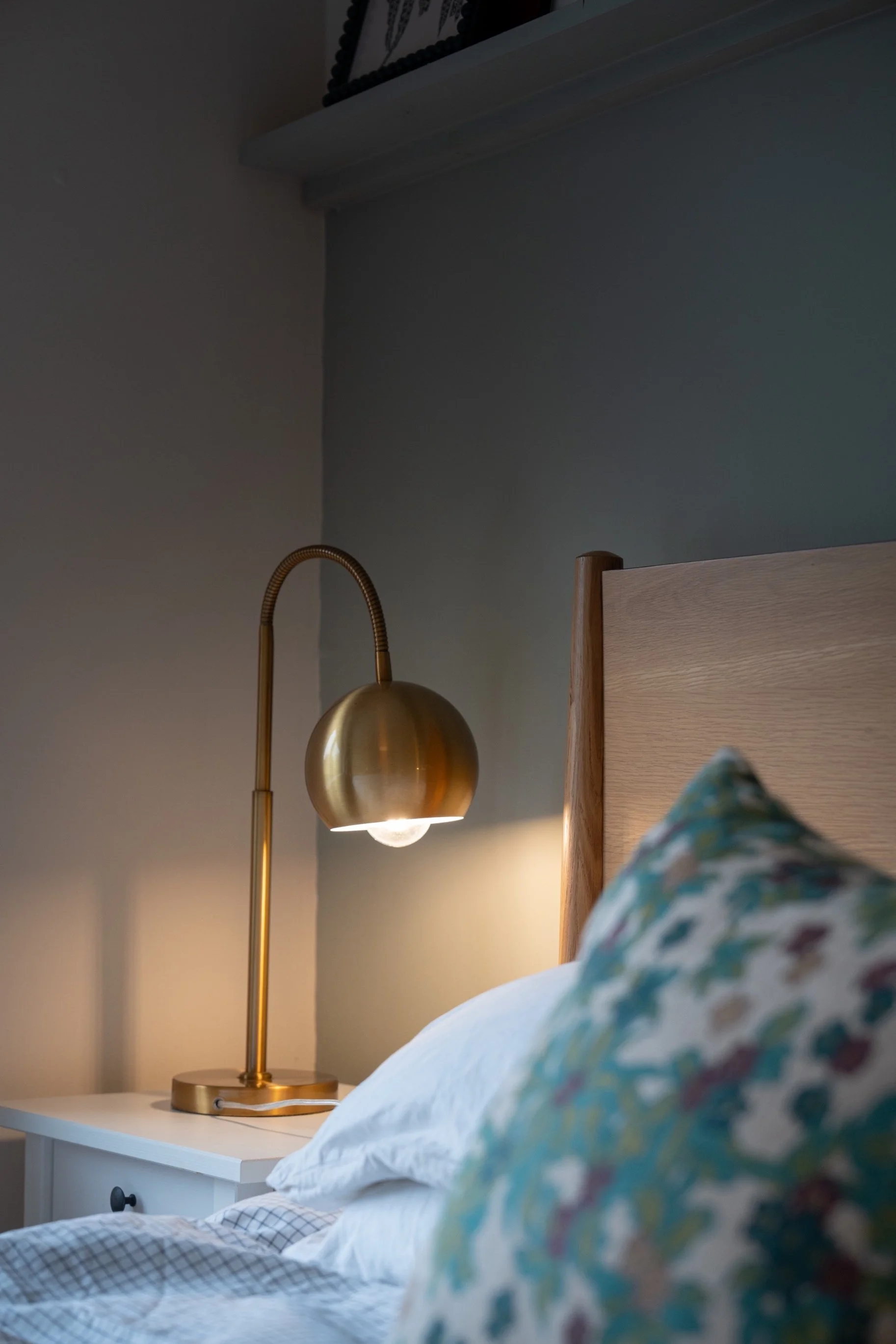 Minimalist bedroom detail with brass bedside lamp, upholstered headboard, and soft blue-grey walls for a calming modern retreat.