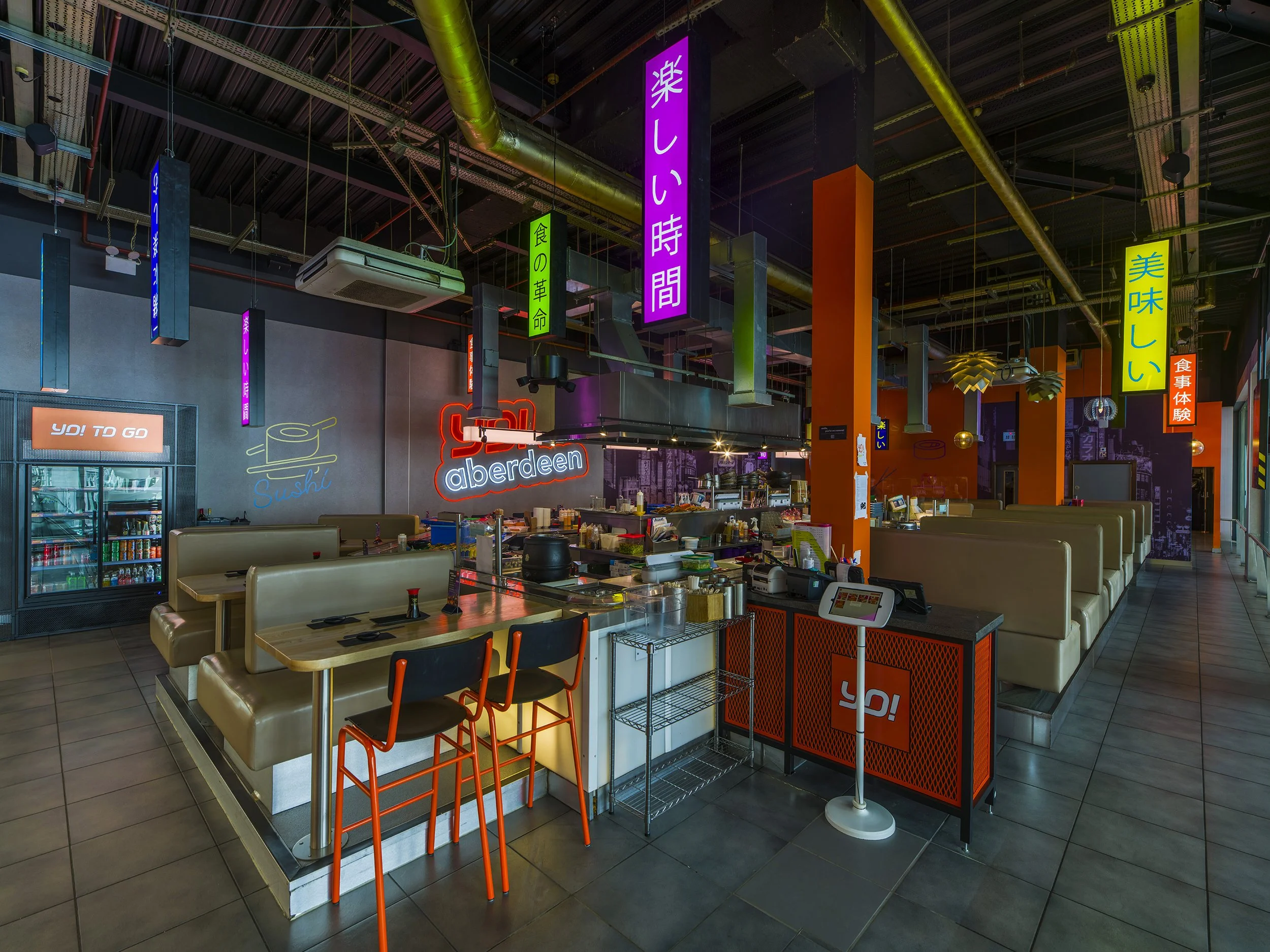 Contemporary sushi restaurant interior with neon signage, timber bar seating, and vibrant atmospheric lighting at YO! Aberdeen.