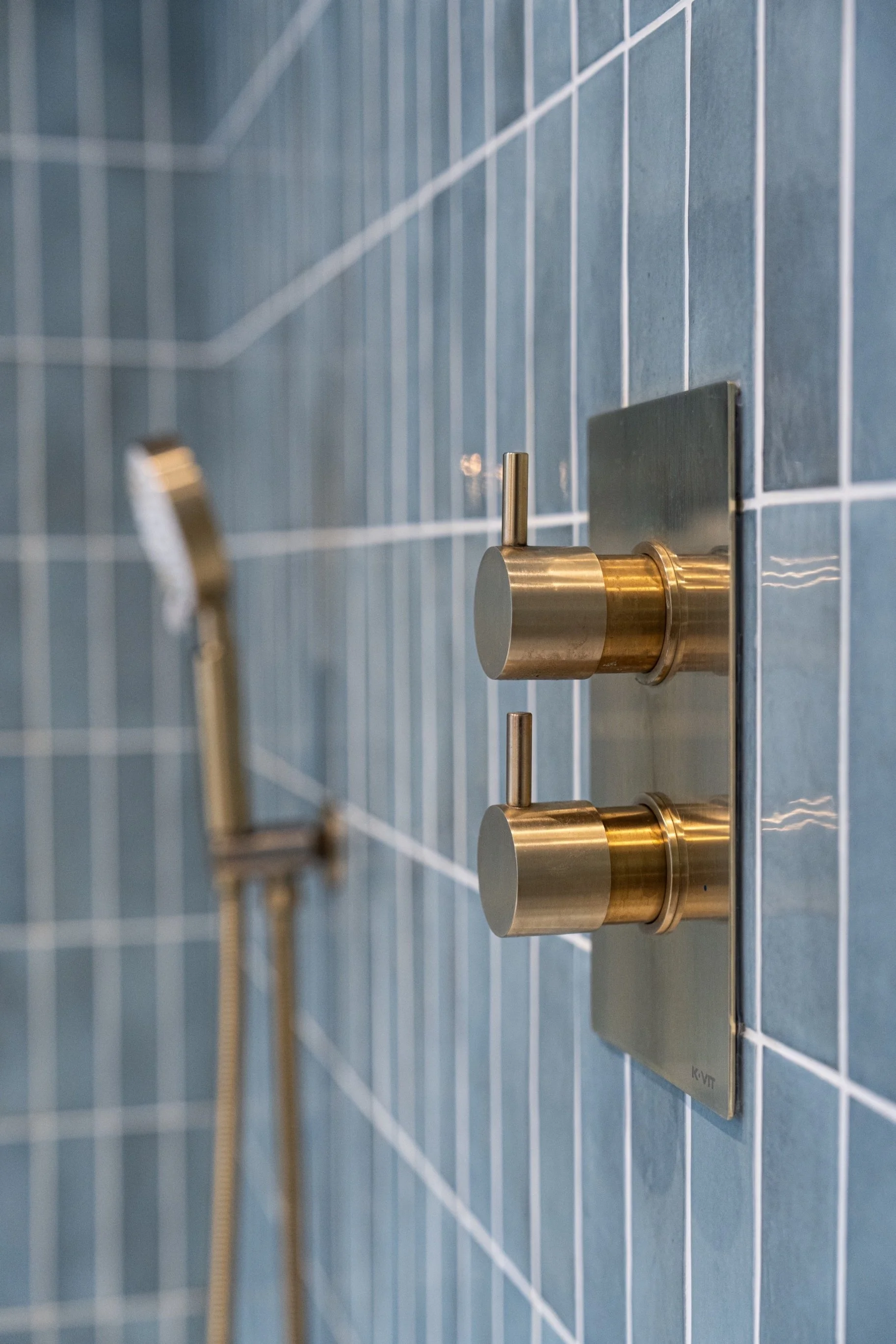 Luxury bathroom detail featuring brushed brass shower controls and blue vertical subway tiles in a modern spa-inspired bathroom design.
