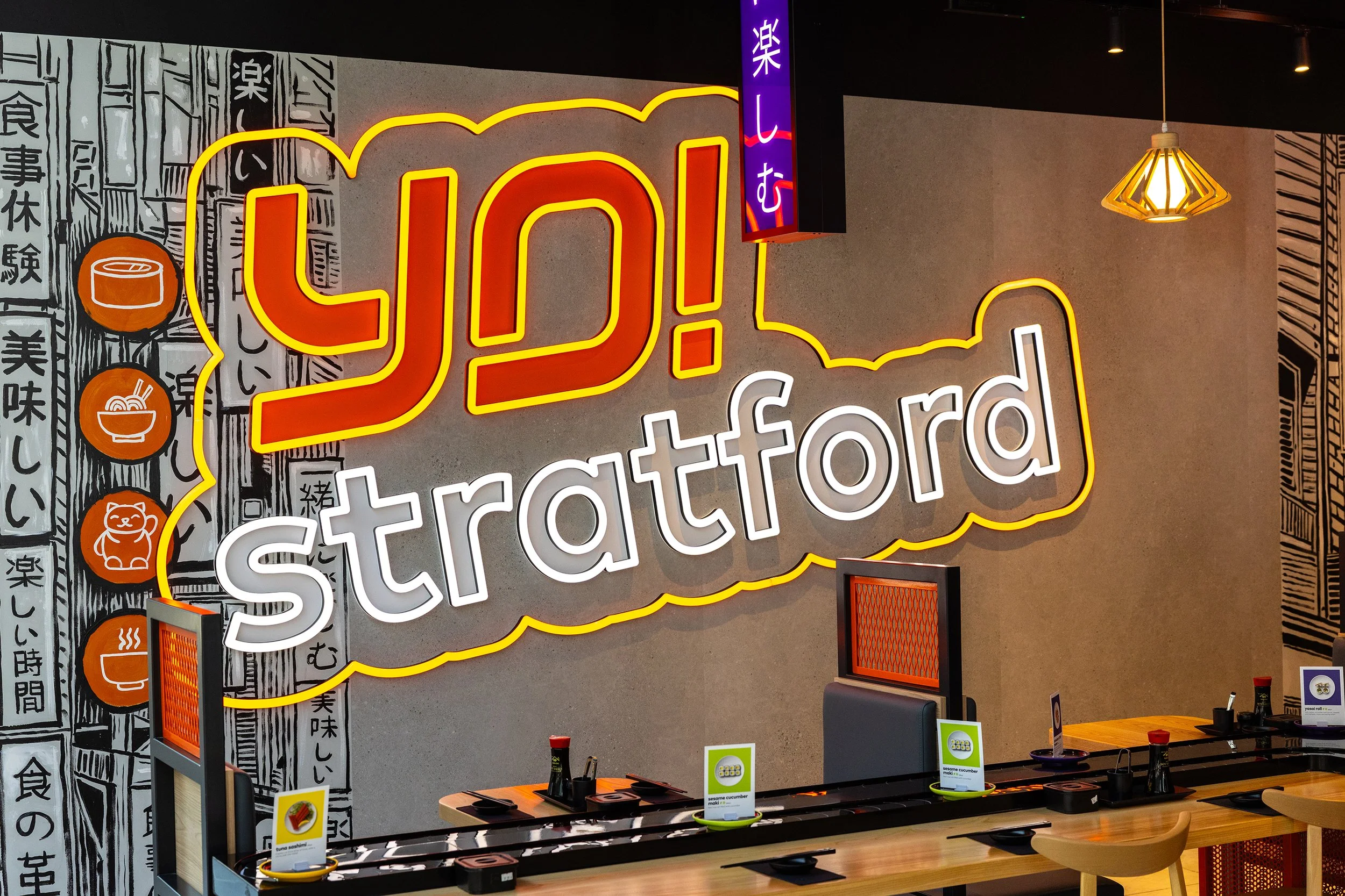 Illuminated YO! Stratford signage with bold neon branding and contemporary Japanese restaurant interiors in London.