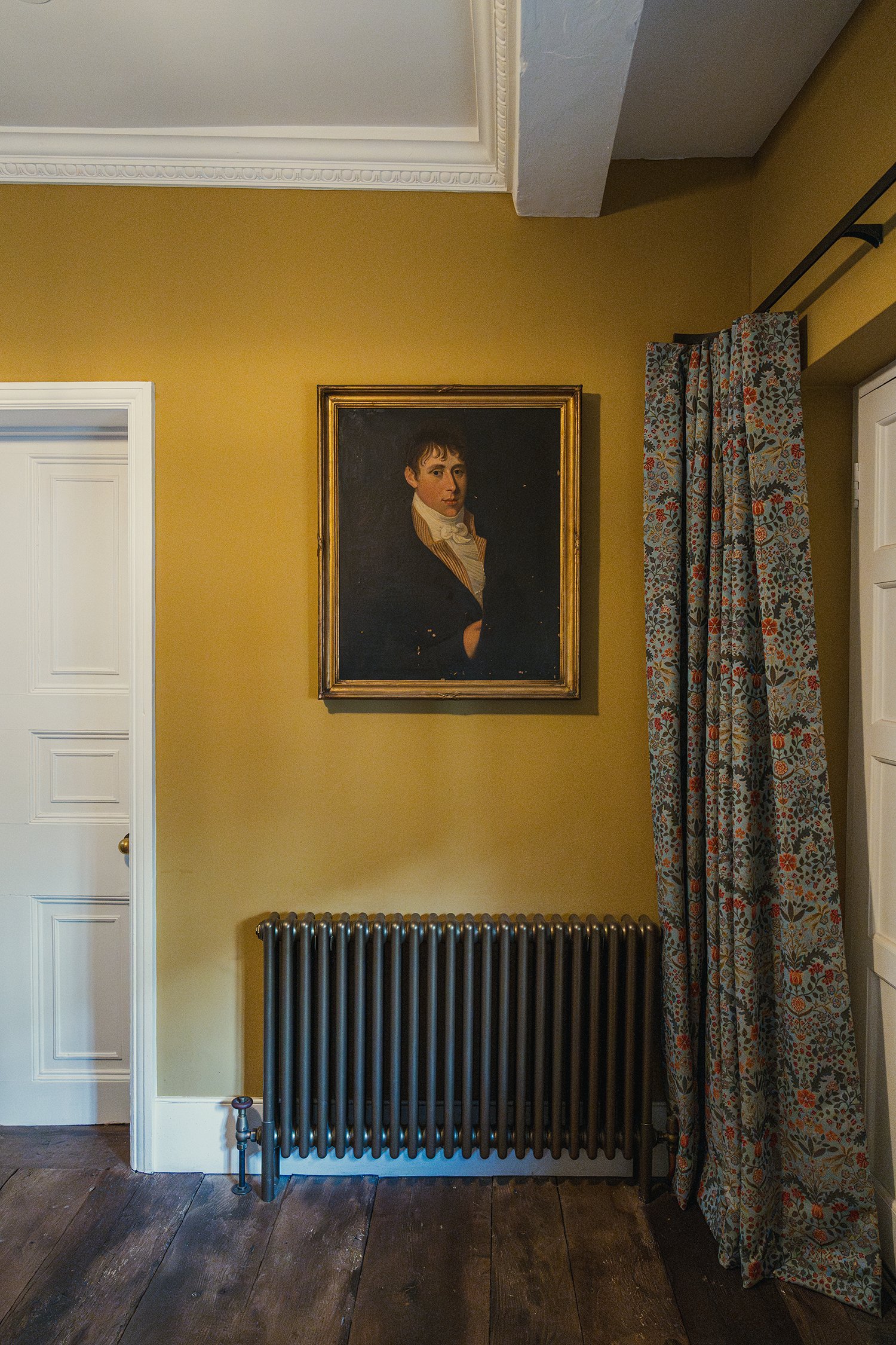 Warm and atmospheric hallway with ochre walls, vintage portrait artwork, dark timber flooring, and layered heritage-inspired styling.