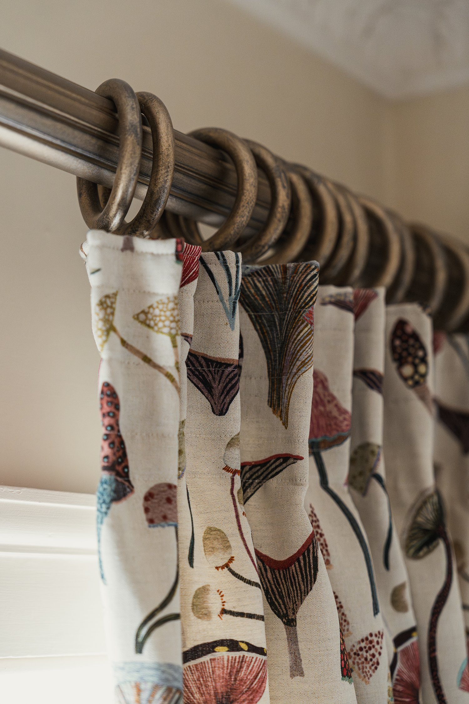 Patterned botanical curtains on antique brass curtain rings bringing colour, craftsmanship, and personality to a townhouse guest room.