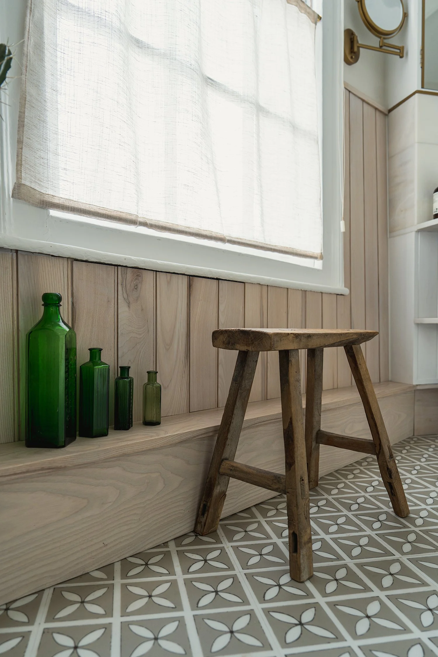 Townhouse shower room with patterned floor tiles, rustic wooden stool, green glass bottles, and natural textures creating a calm spa-inspired atmosphere.