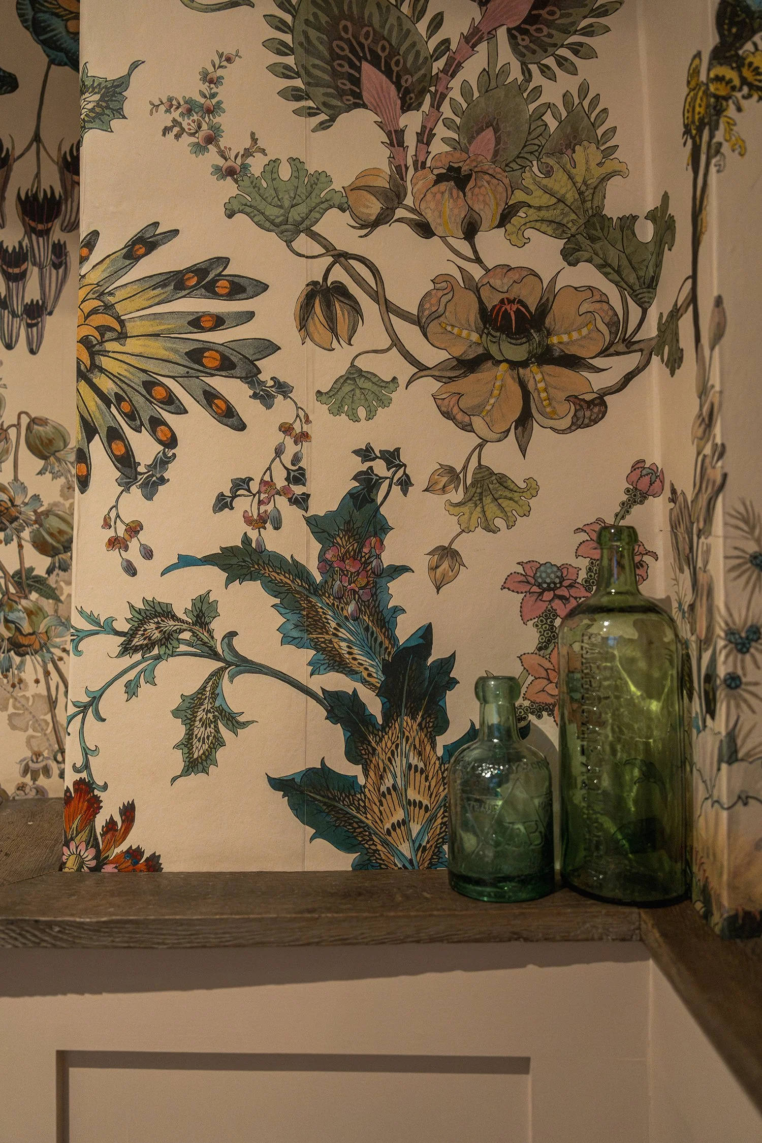 Close-up of richly patterned botanical wallpaper with styled glass bottles and layered textures in a characterful townhouse powder room.