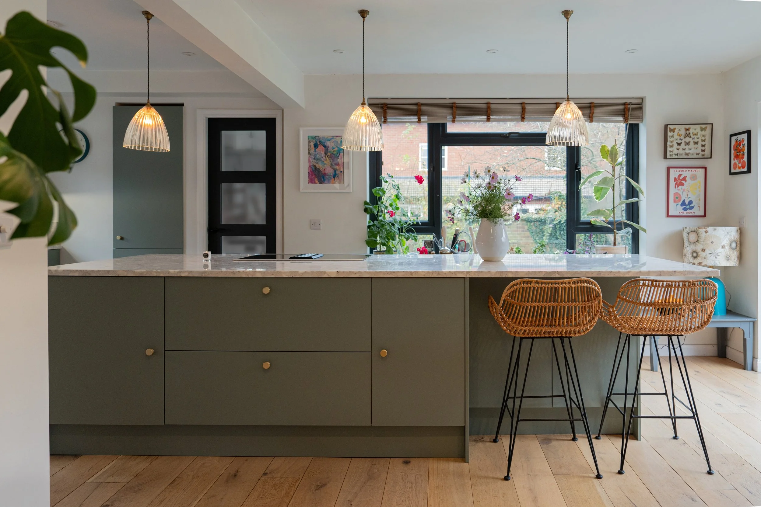 A bright, open kitchen and dining area with floral wallpaper, a white marble kitchen island with a bowl of apples on it, a dining table with blue chairs, and pendant lights hanging from the ceiling.