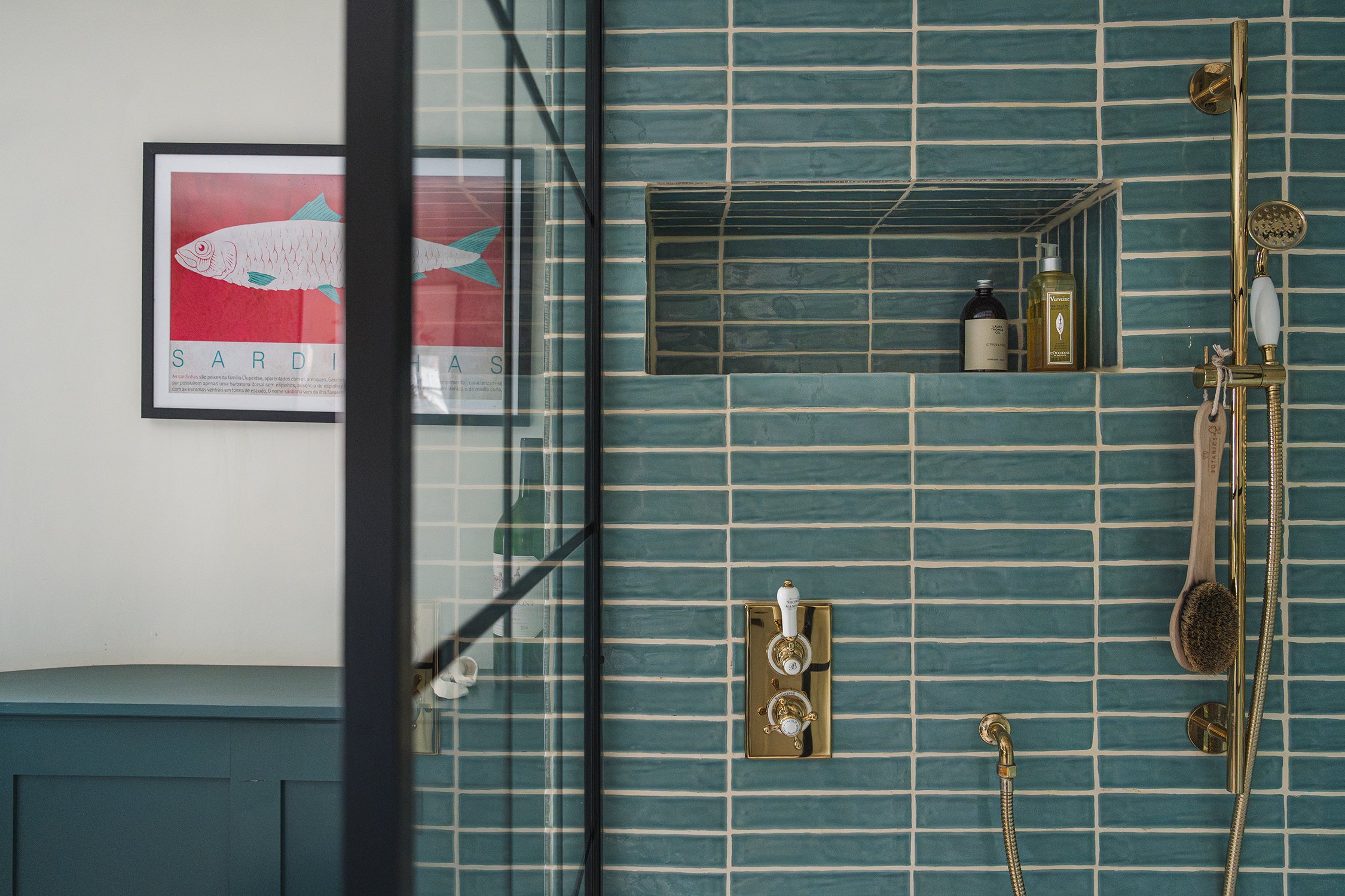 Walk-in shower with blue glazed tiles, brass shower fittings, built-in niche shelving, and framed artwork in a characterful townhouse bathroom.