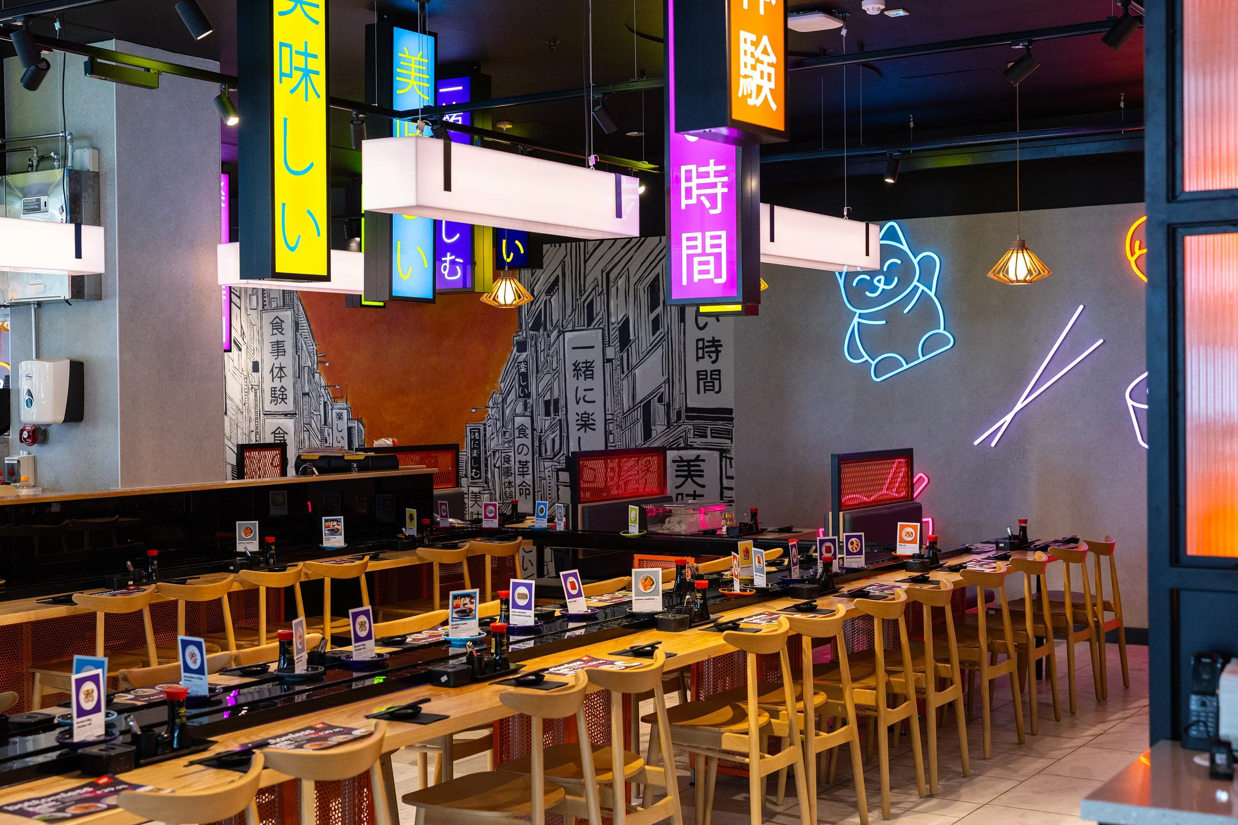 Contemporary Japanese restaurant interior with colourful illuminated signage, conveyor belt dining, and modern seating at YO! Sushi Stratford.