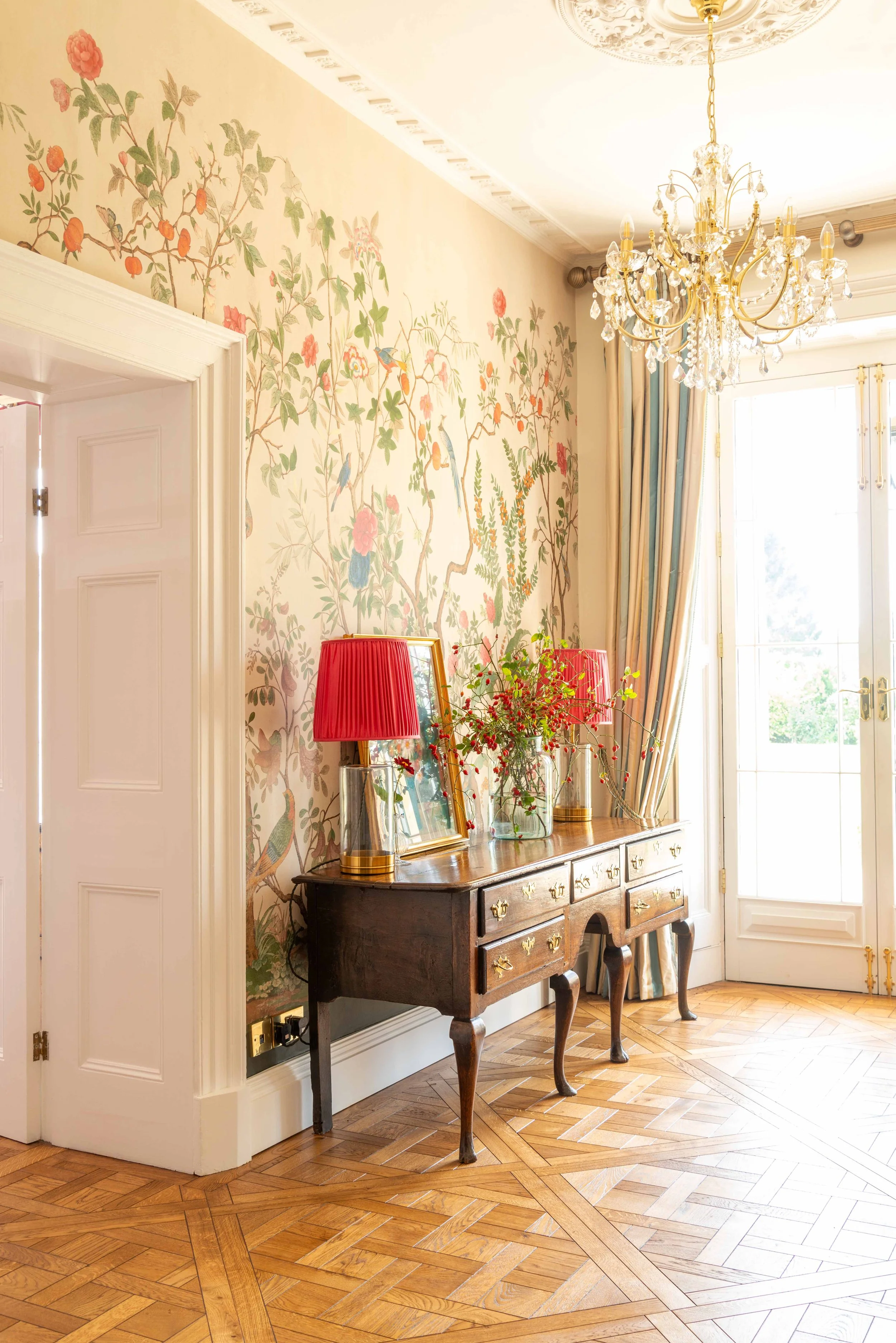 Elegant Georgian hallway with parquet flooring, botanical wallpaper, crystal chandelier, and antique console table styled with fresh flowers.