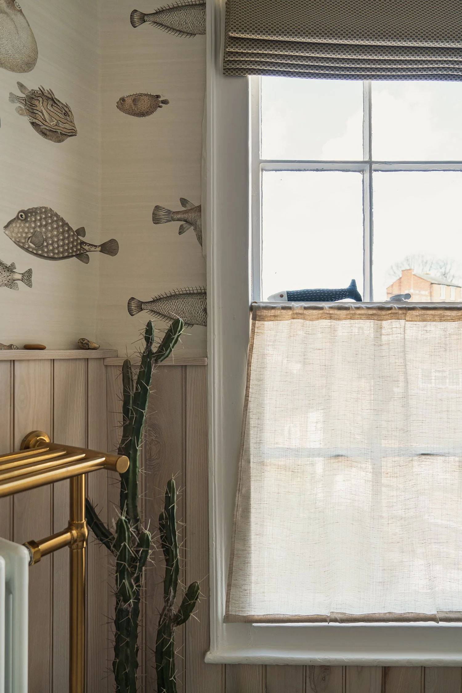 Elegant townhouse bathroom with textured fish wallpaper, soft natural light, brass fittings, and layered neutral tones for a relaxed modern feel.