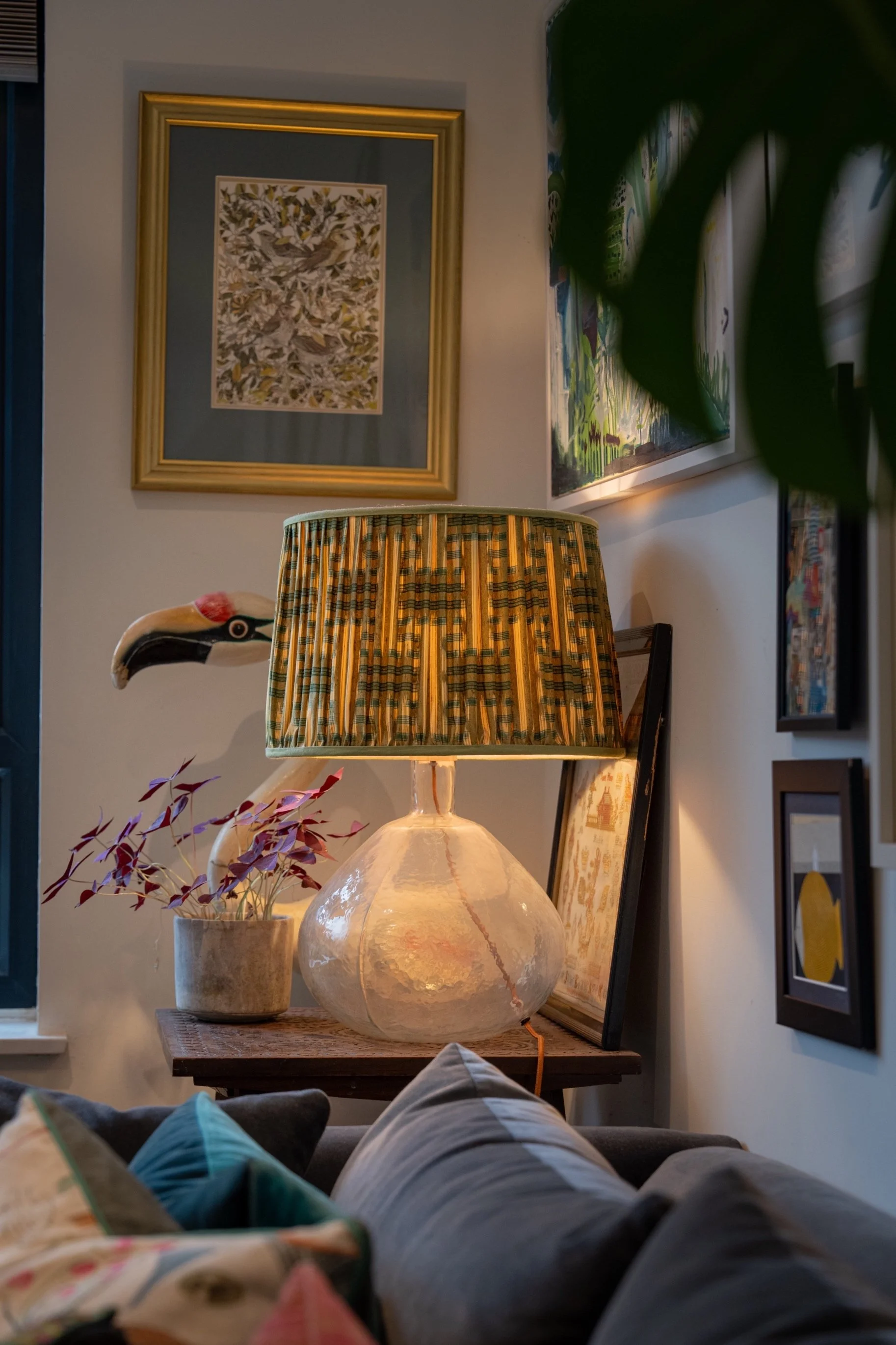 Stylish living room corner with textured table lamp, framed artwork, layered cushions, and warm ambient lighting in a modern home.