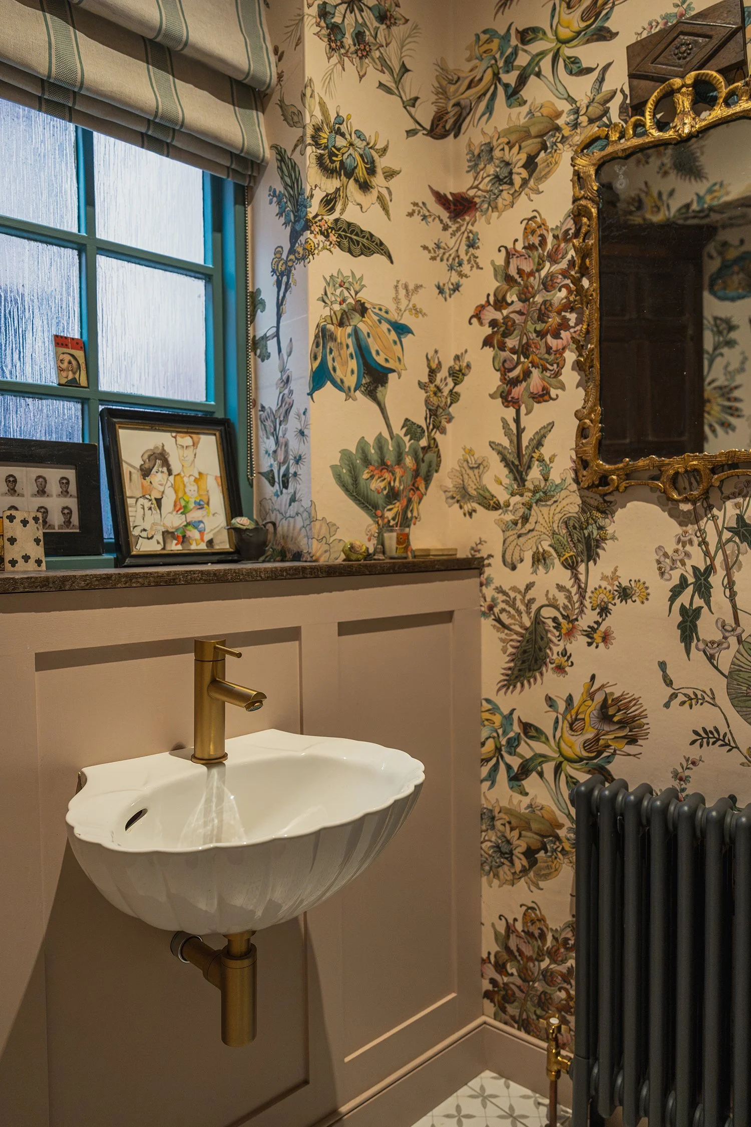 Elegant downstairs powder room with sculptural wall-mounted basin, brass tapware, botanical wallpaper, and curated vintage styling.
