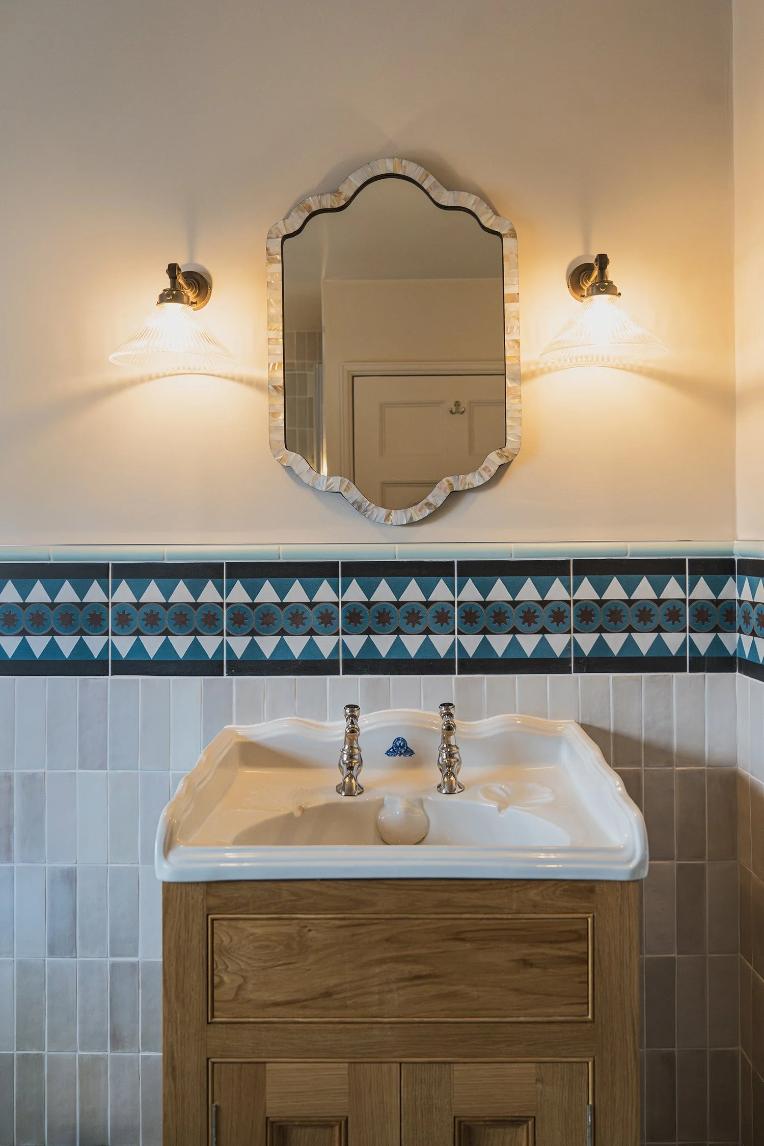 Heritage-inspired bathroom vanity with oak cabinetry, scalloped mirror, and decorative blue tile border in a refined townhouse scheme.