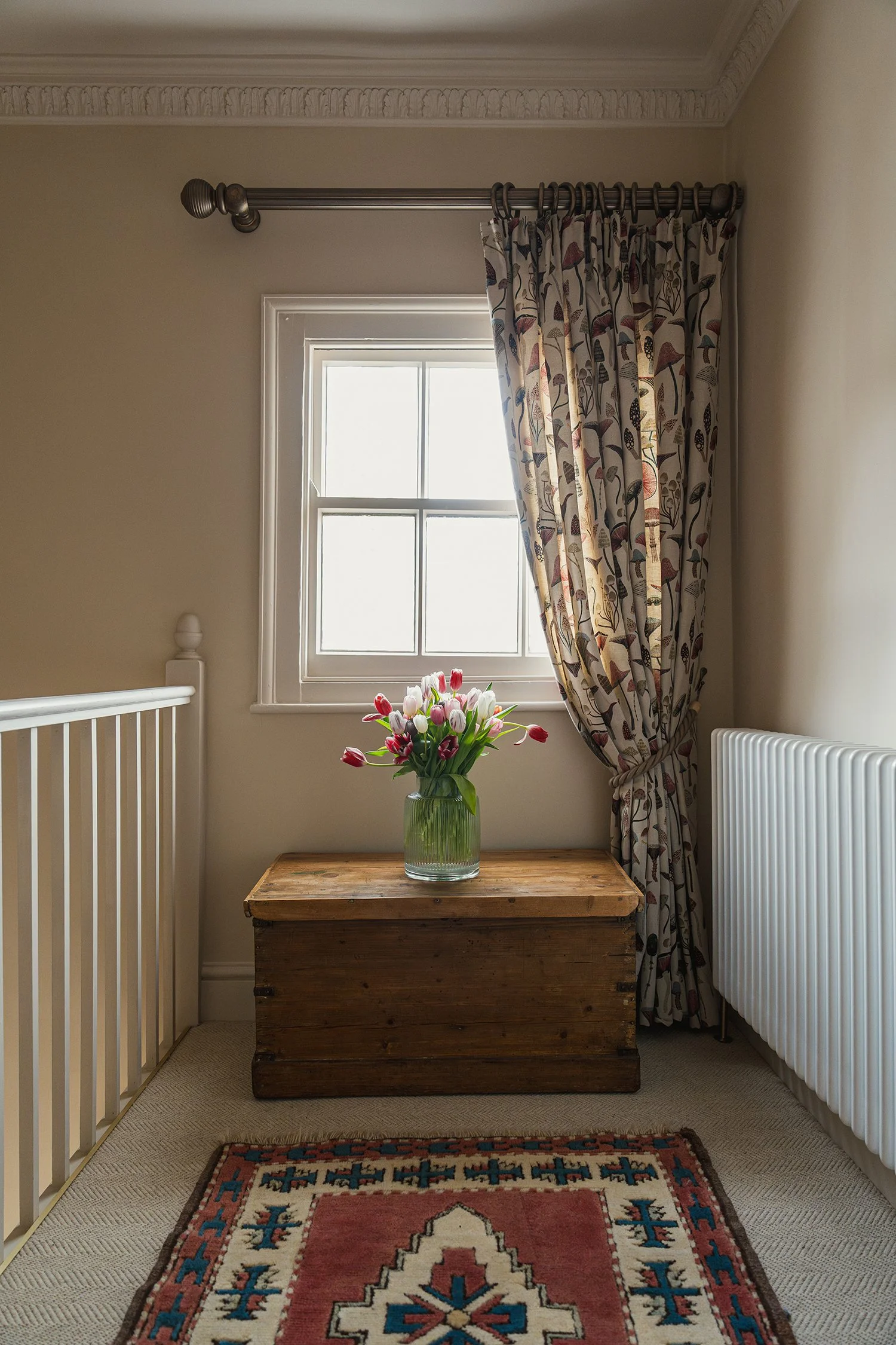 Cozy townhouse guest bedroom corner with patterned curtains, vintage chest, fresh flowers, and heritage-inspired styling details.