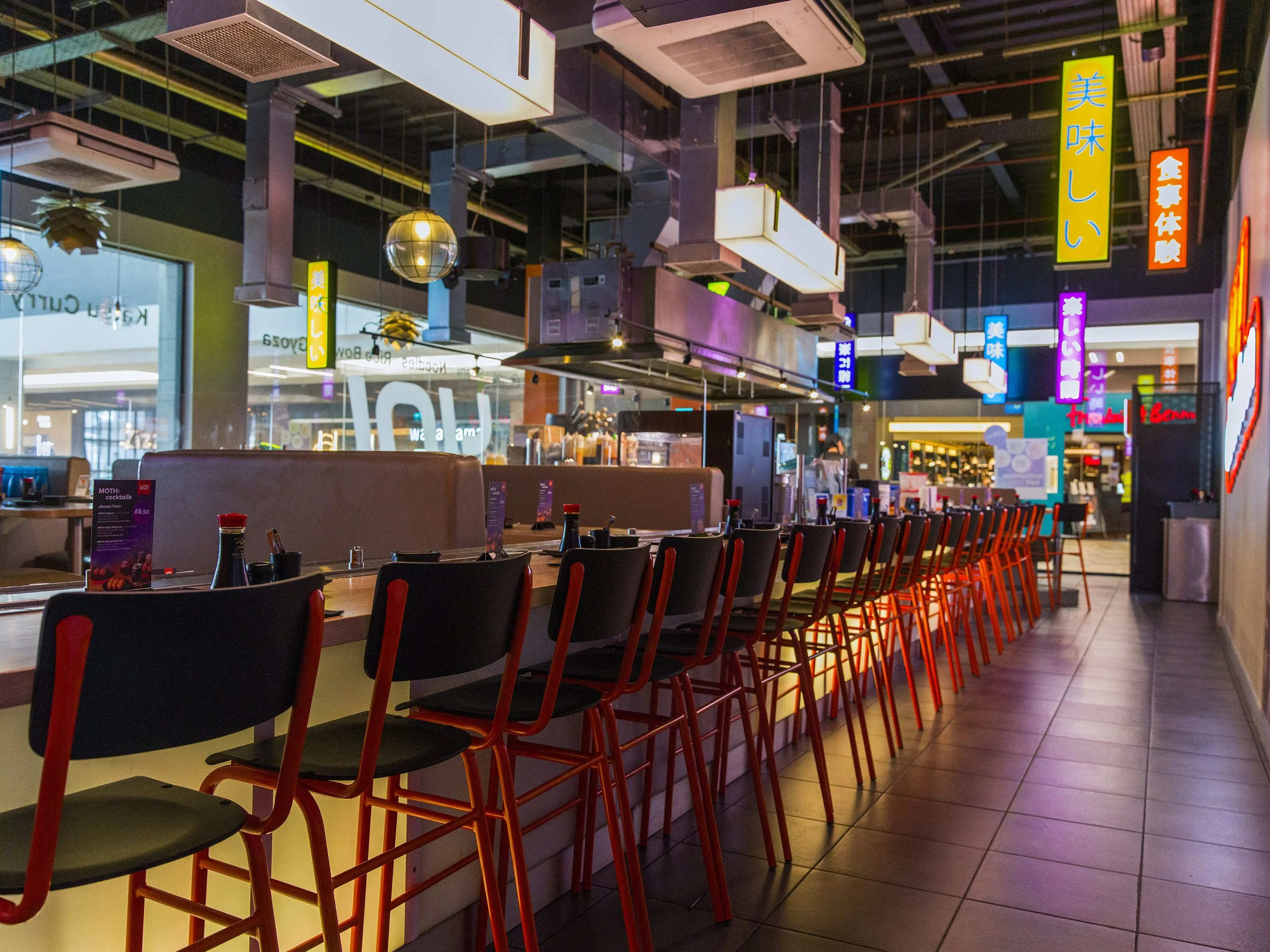 Open sushi counter and bar seating with industrial-style lighting and colourful neon signage in YO! Aberdeen restaurant.