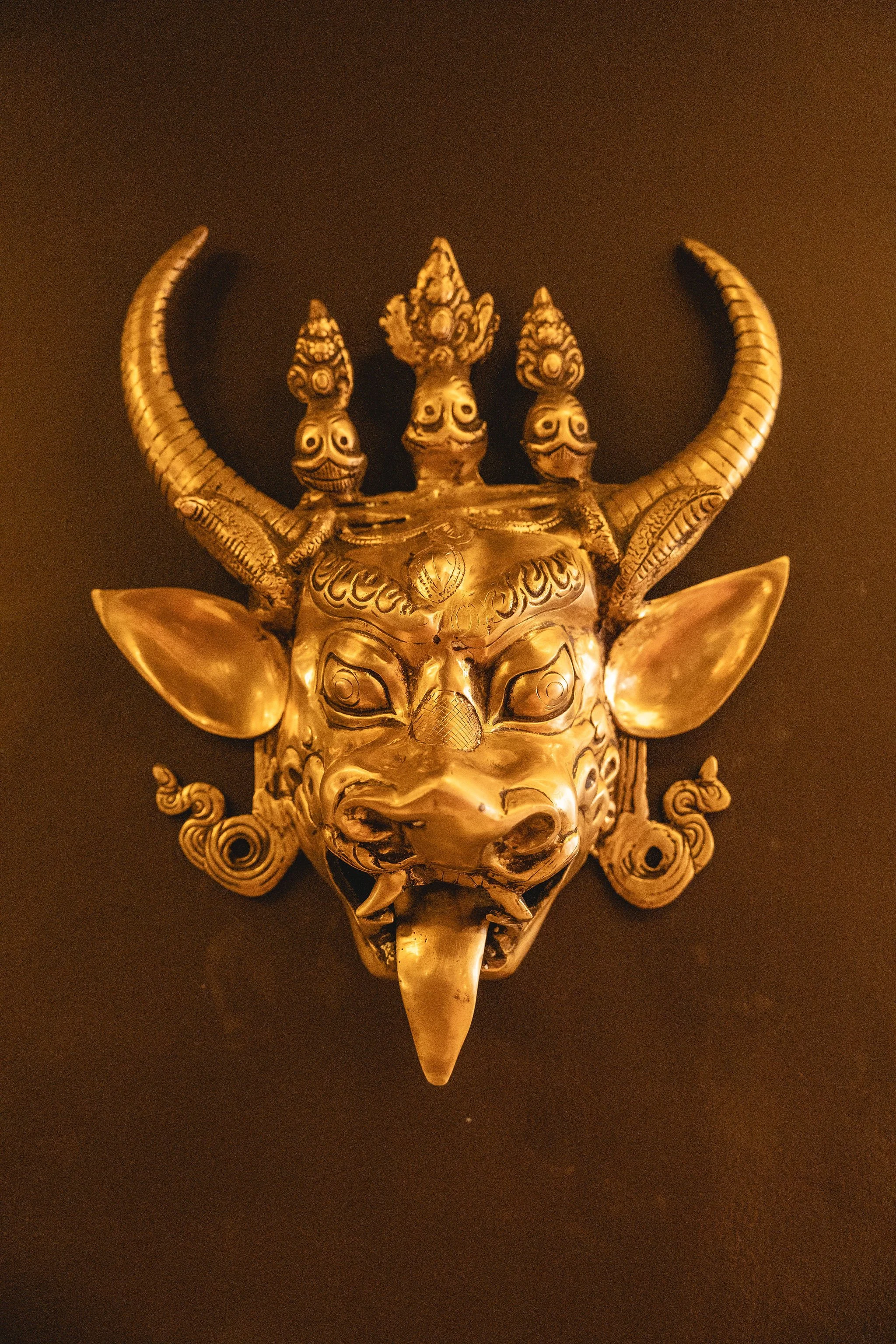 A golden sculpture of a mythological creature with a fierce face, large horns, and intricate decorative details.