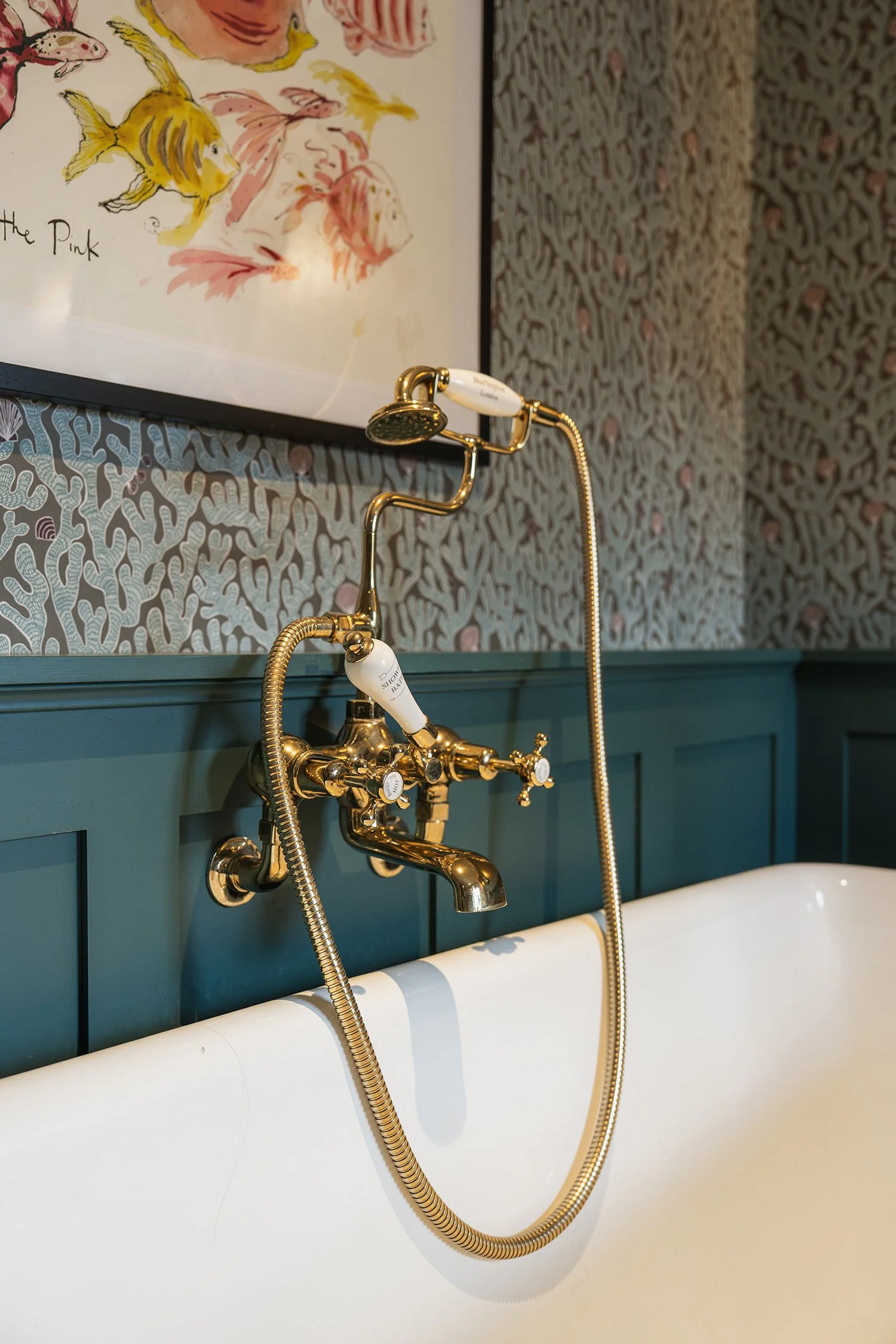 Classic brass bath filler and handheld shower detail styled against patterned wallpaper in a sophisticated townhouse bathroom.