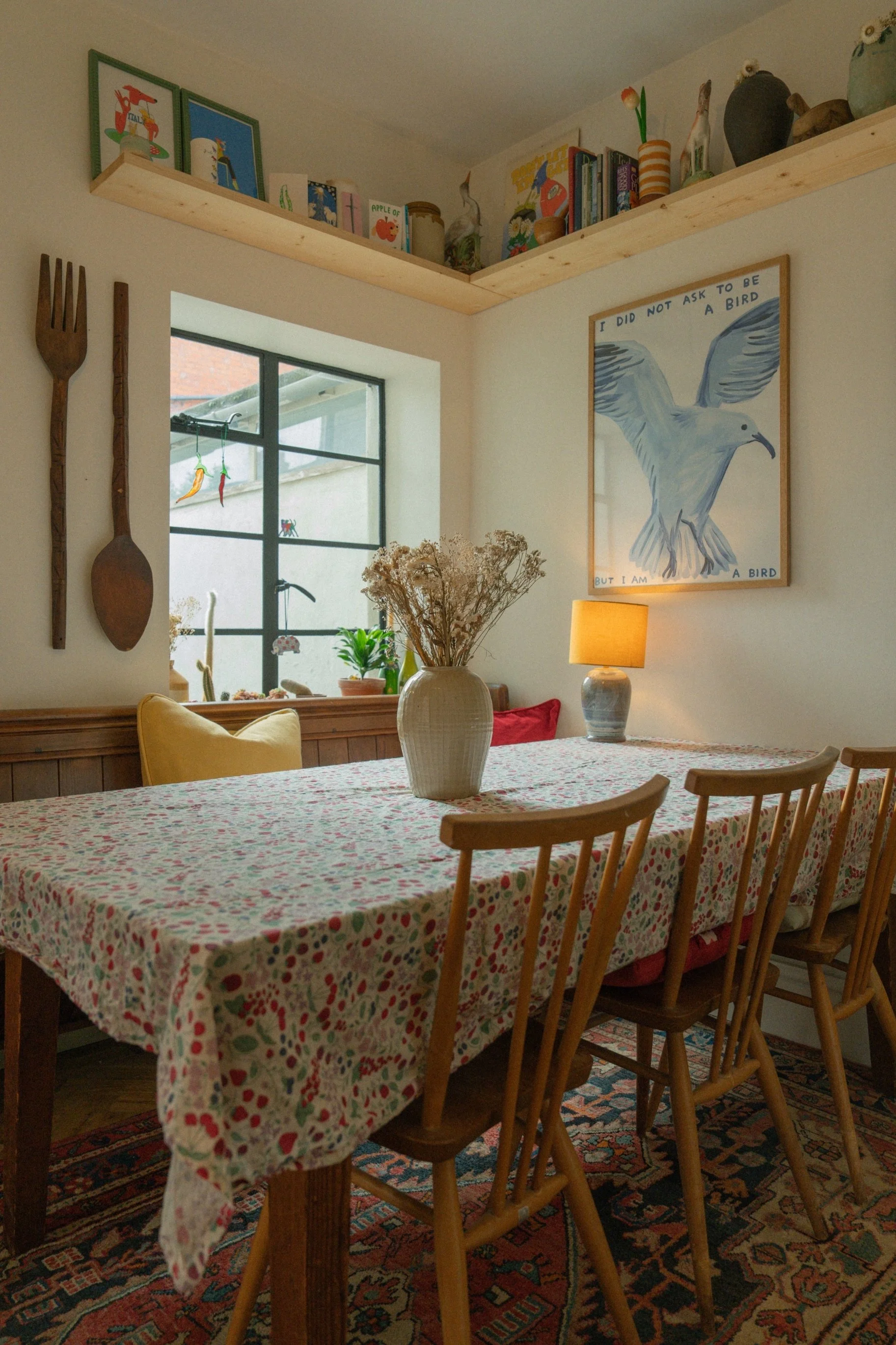Characterful Edwardian dining space with floral tablecloth, vintage furniture, layered artwork, and natural light creating a welcoming family interior.