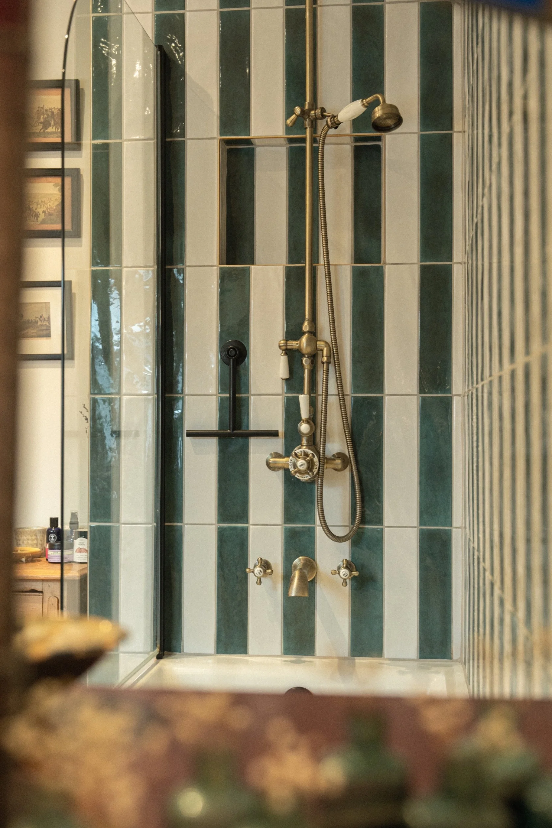 Walk-in shower with bold striped green tiles and classic brass fittings bringing character and craftsmanship to an Edwardian bathroom design.