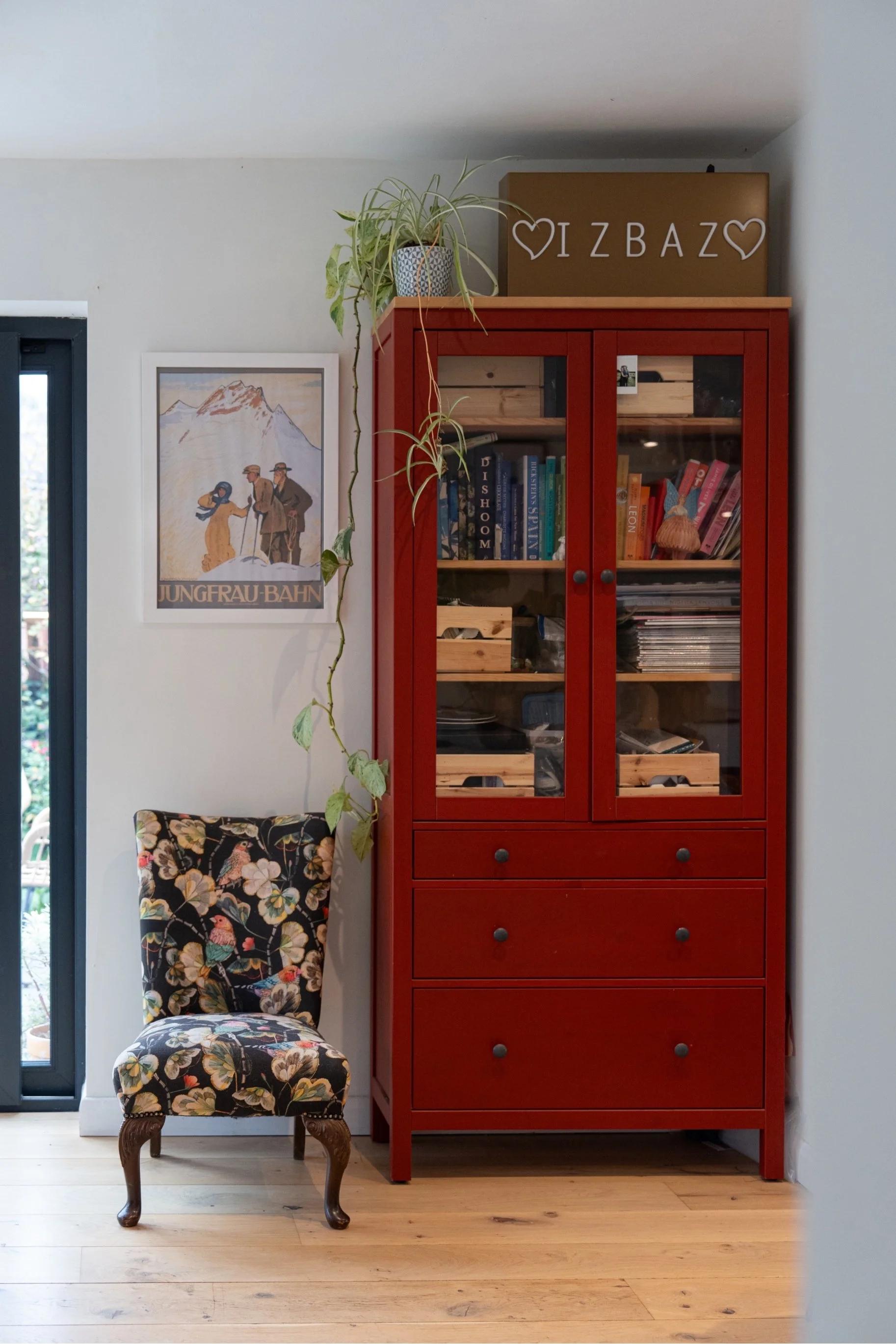 Eclectic living space with vintage floral armchair, bold red display cabinet, indoor plants, and curated contemporary home decor.