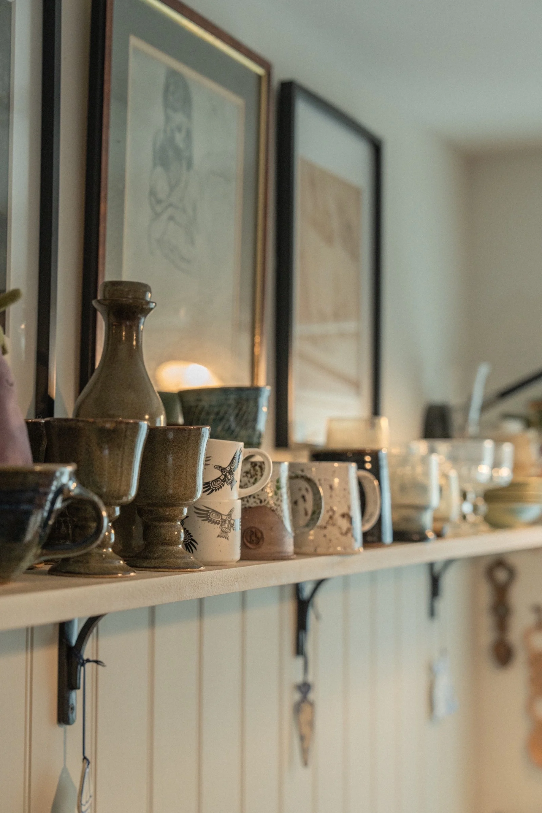 Styled open shelving with handmade ceramics, framed artwork, and soft layered textures in a thoughtfully curated family home.