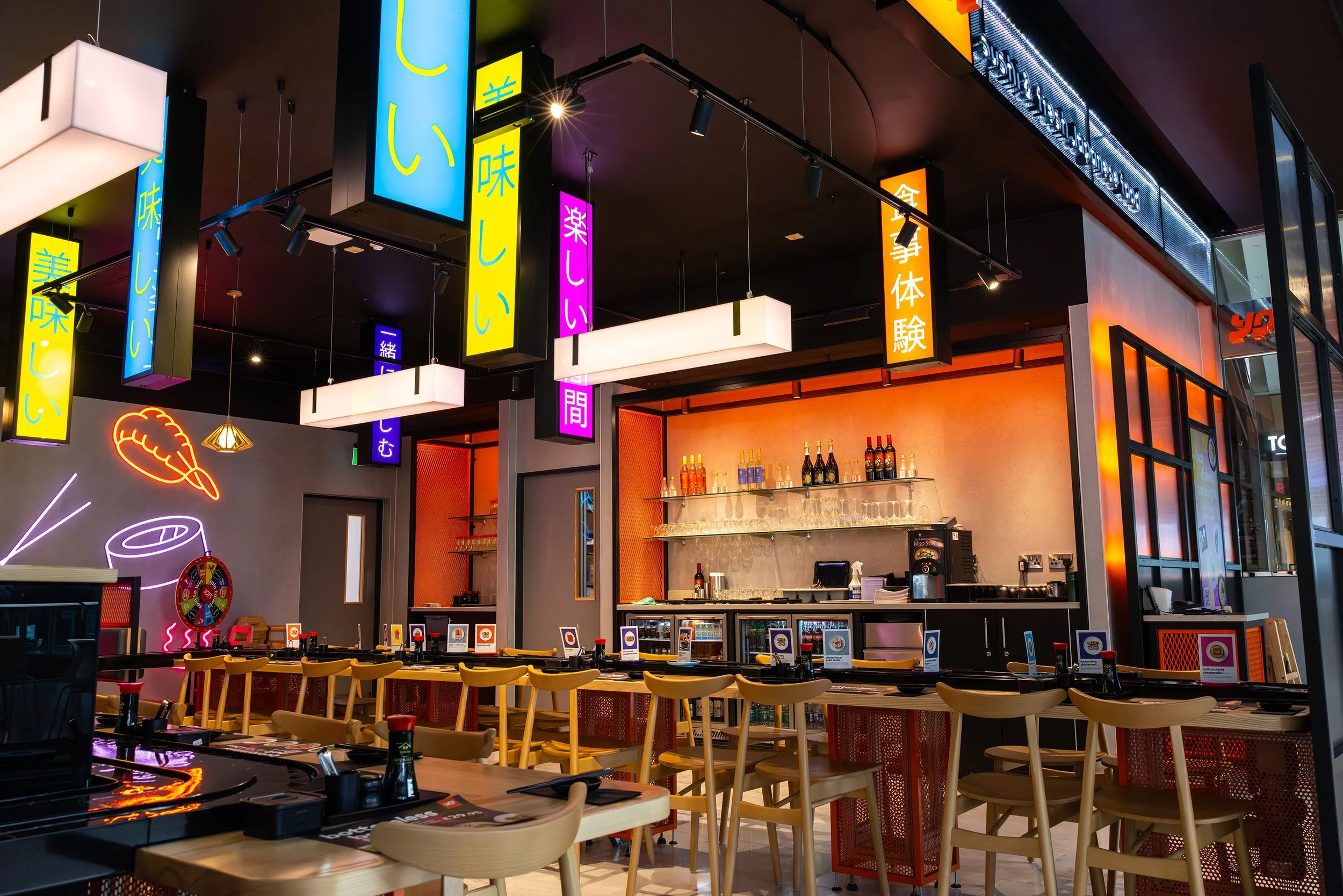 Open-plan YO! Sushi Stratford dining area featuring neon Japanese signage, industrial-style lighting, and contemporary restaurant interiors.