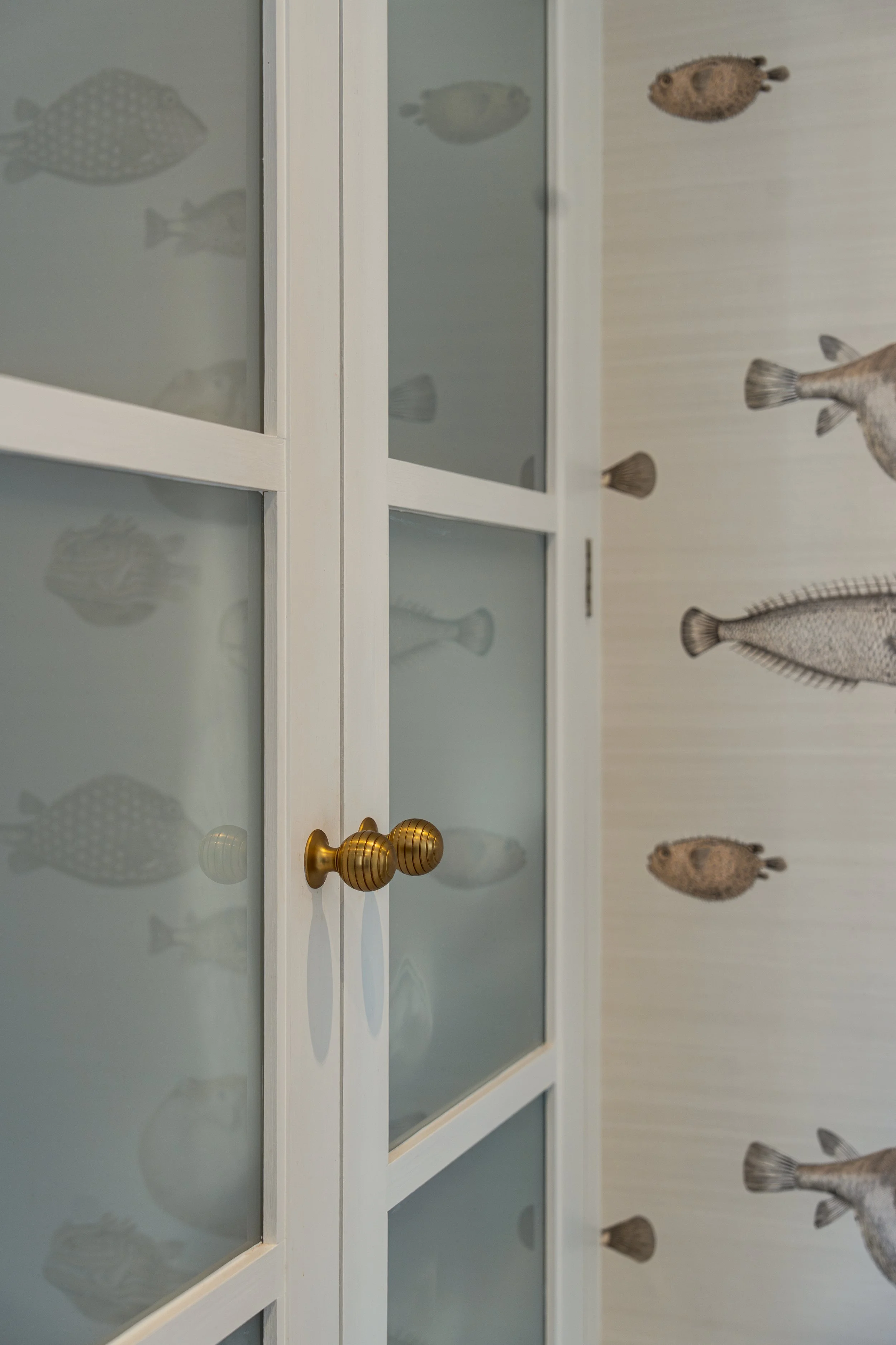 Bespoke bathroom cabinetry with frosted glass doors, brass handles, and whimsical fish wallpaper in a characterful townhouse shower room.