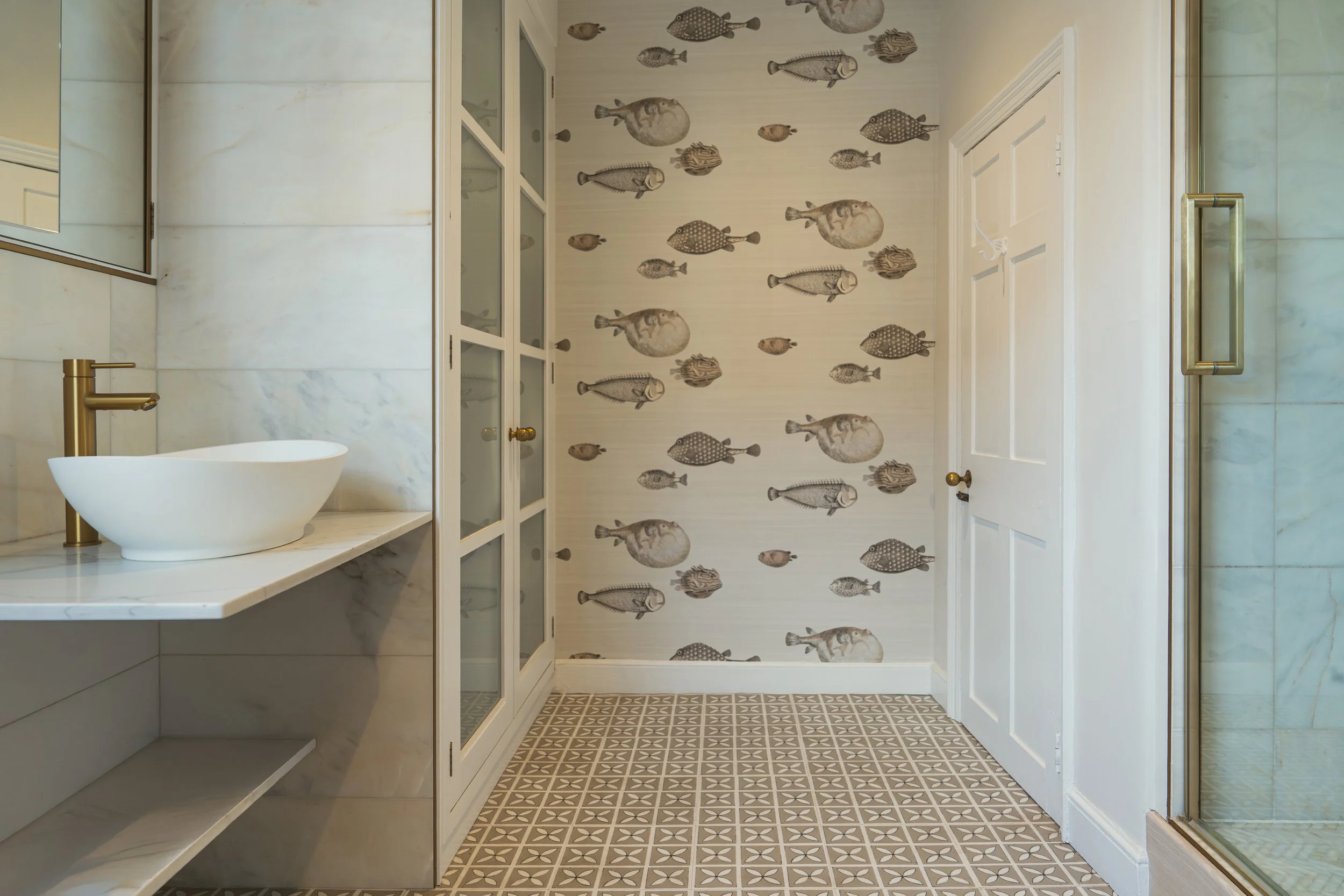 Full view of a luxury townhouse shower room featuring bespoke vanity, patterned tiles, brass detailing, and playful fish wallpaper throughout.