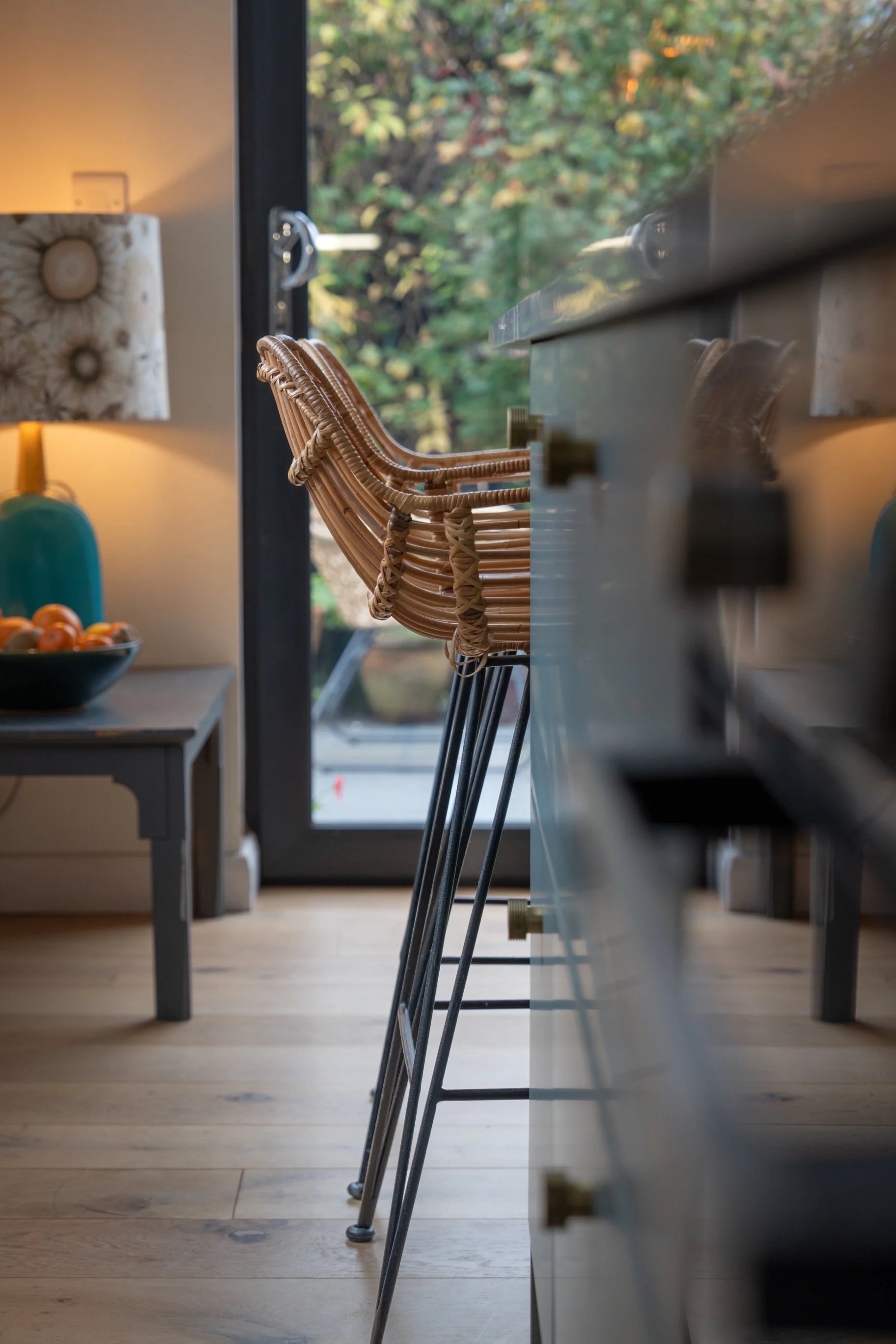 Modern kitchen and dining area with woven bar stool, natural wood flooring, and soft-focus contemporary interior styling.