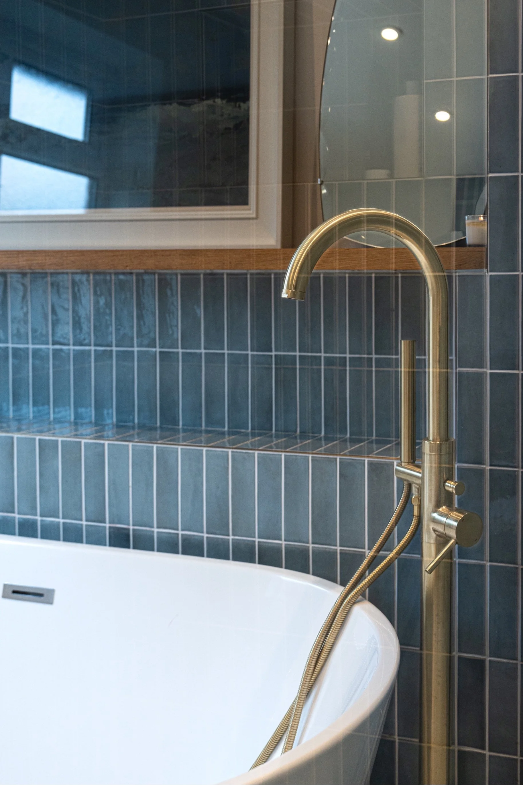 Contemporary freestanding bathtub with brass tapware and blue tiled bathroom walls in a luxury spa-style interior.