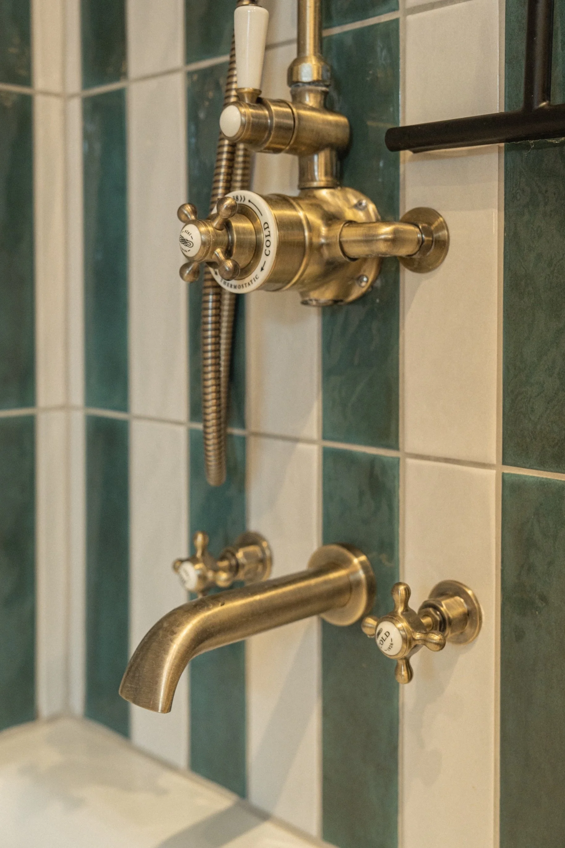 Traditional brass shower fittings set against striking green striped tiles in a thoughtfully designed Edwardian townhouse bathroom.