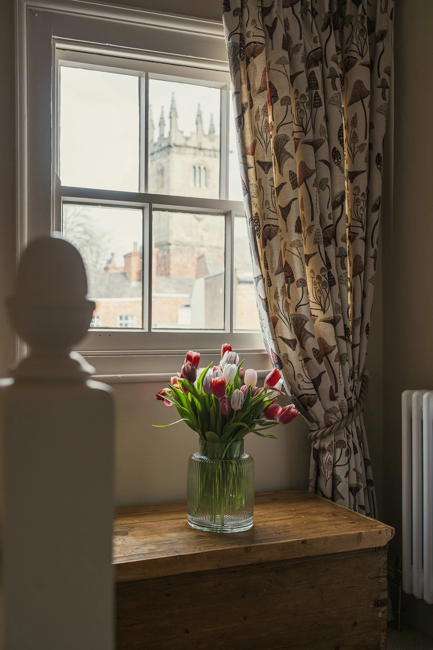 Fresh tulips styled beside patterned curtains and traditional sash window in a warm, characterful townhouse interior.