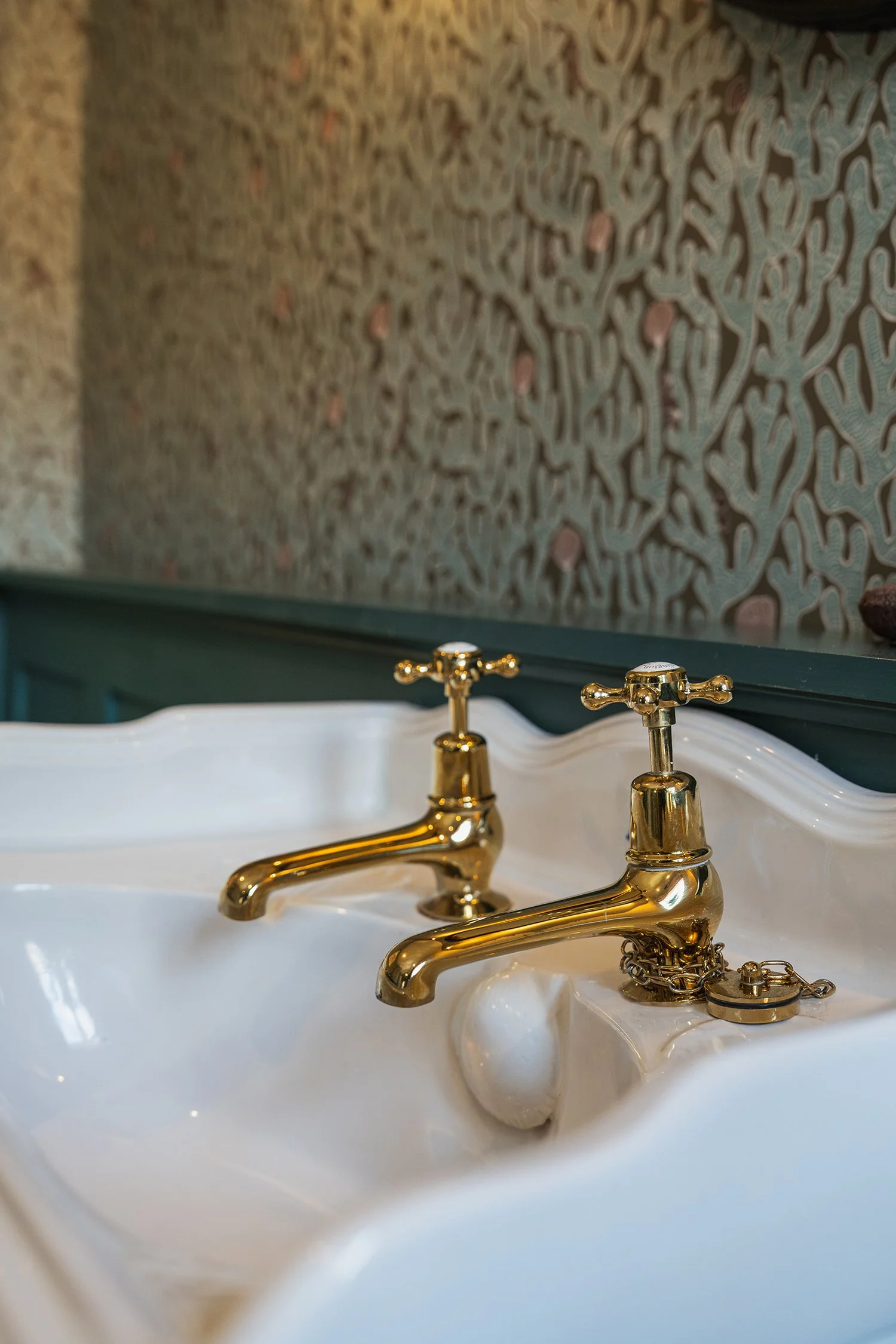 Traditional brass bathroom taps on a vintage-style sink with layered textures and artisan detailing in a luxury townhouse interior.