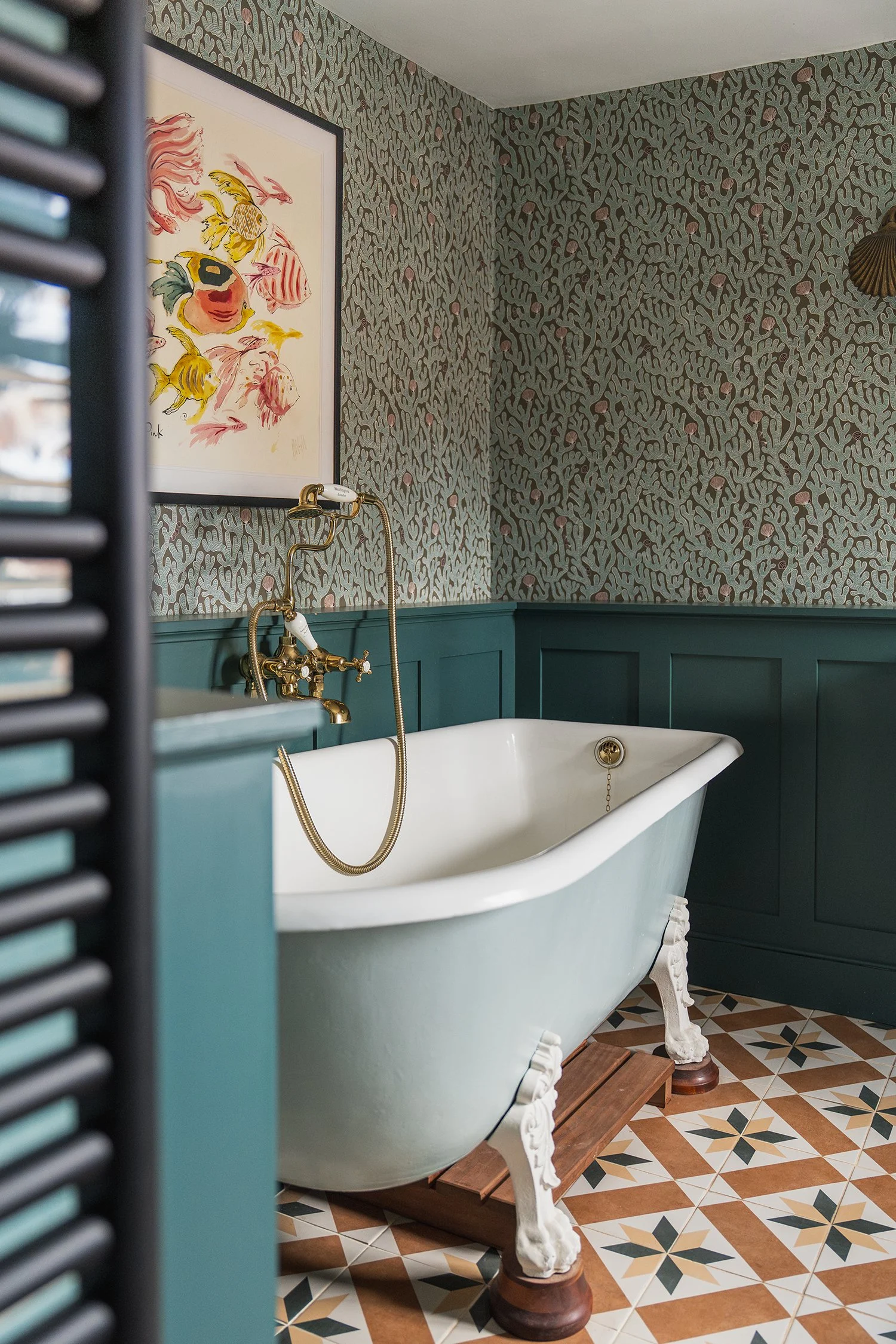 Freestanding clawfoot bath with patterned floor tiles, deep teal panelling, and heritage wallpaper in a thoughtfully curated bathroom design.