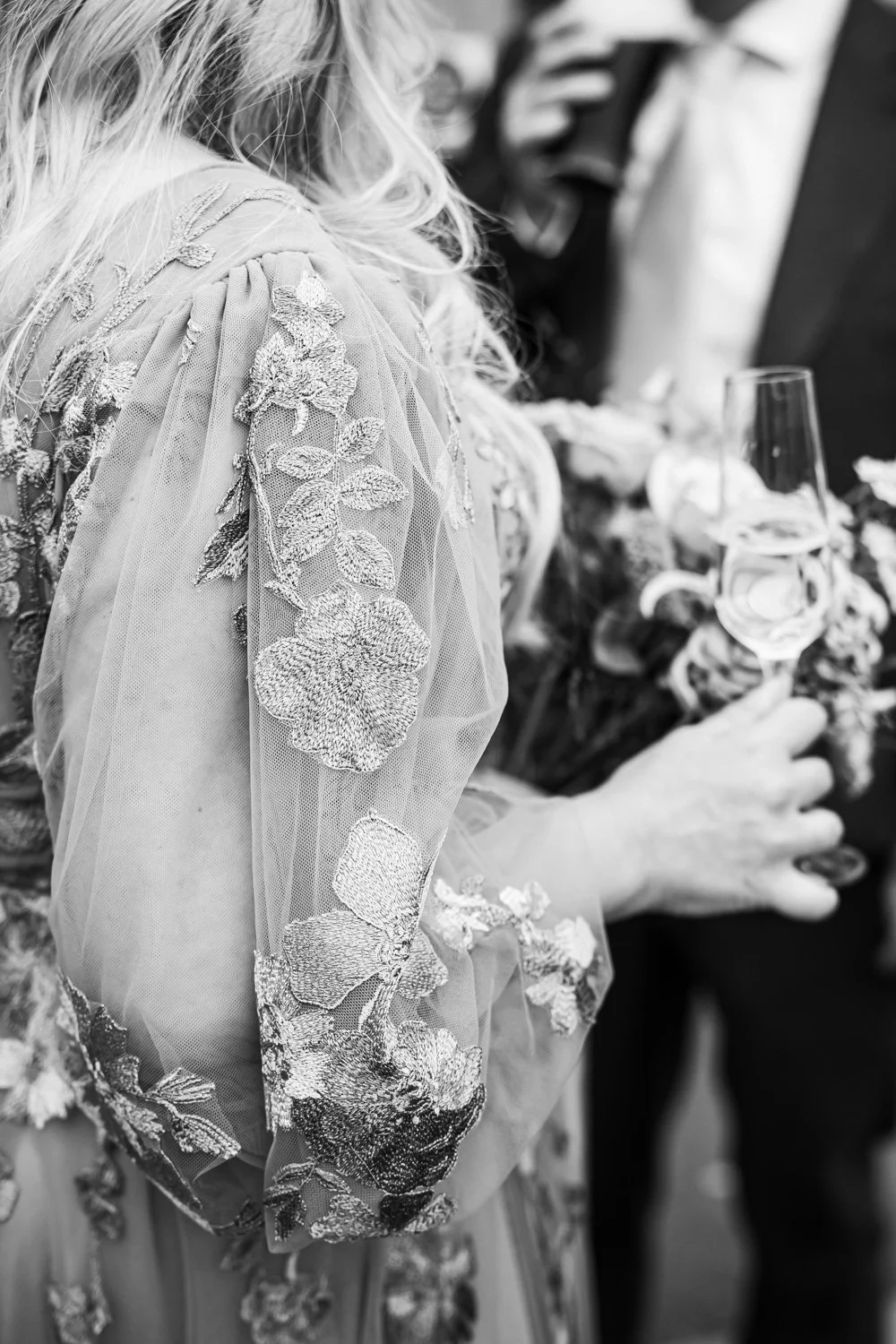 A woman wearing a floral embroidered dress holding a glass of wine at a social gathering.