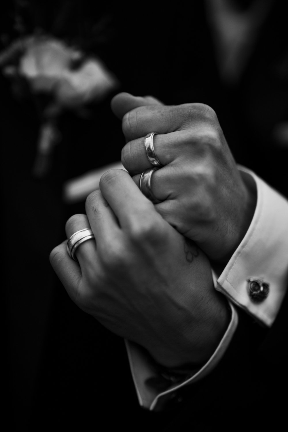 Close-up of a person's hands showing rings, with a blurred flower in the background, in black and white.