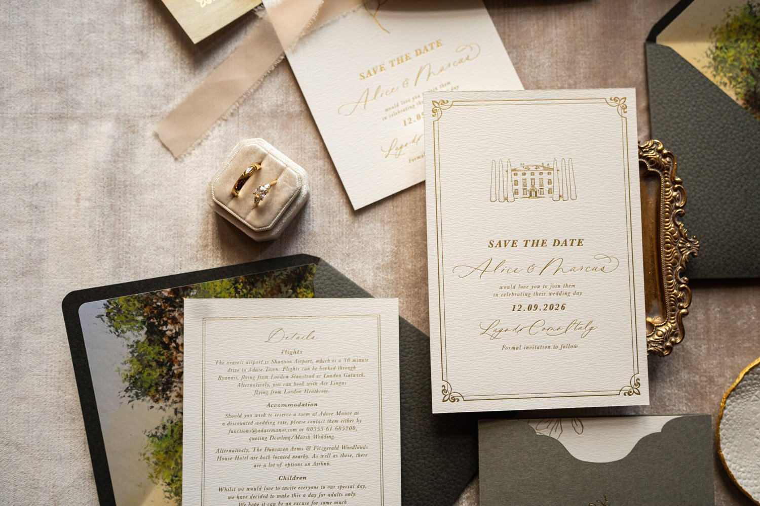 Wedding invitation suite with save the date card, detailed information card, and wedding rings in a small box, arranged on a textured surface with decorative elements.