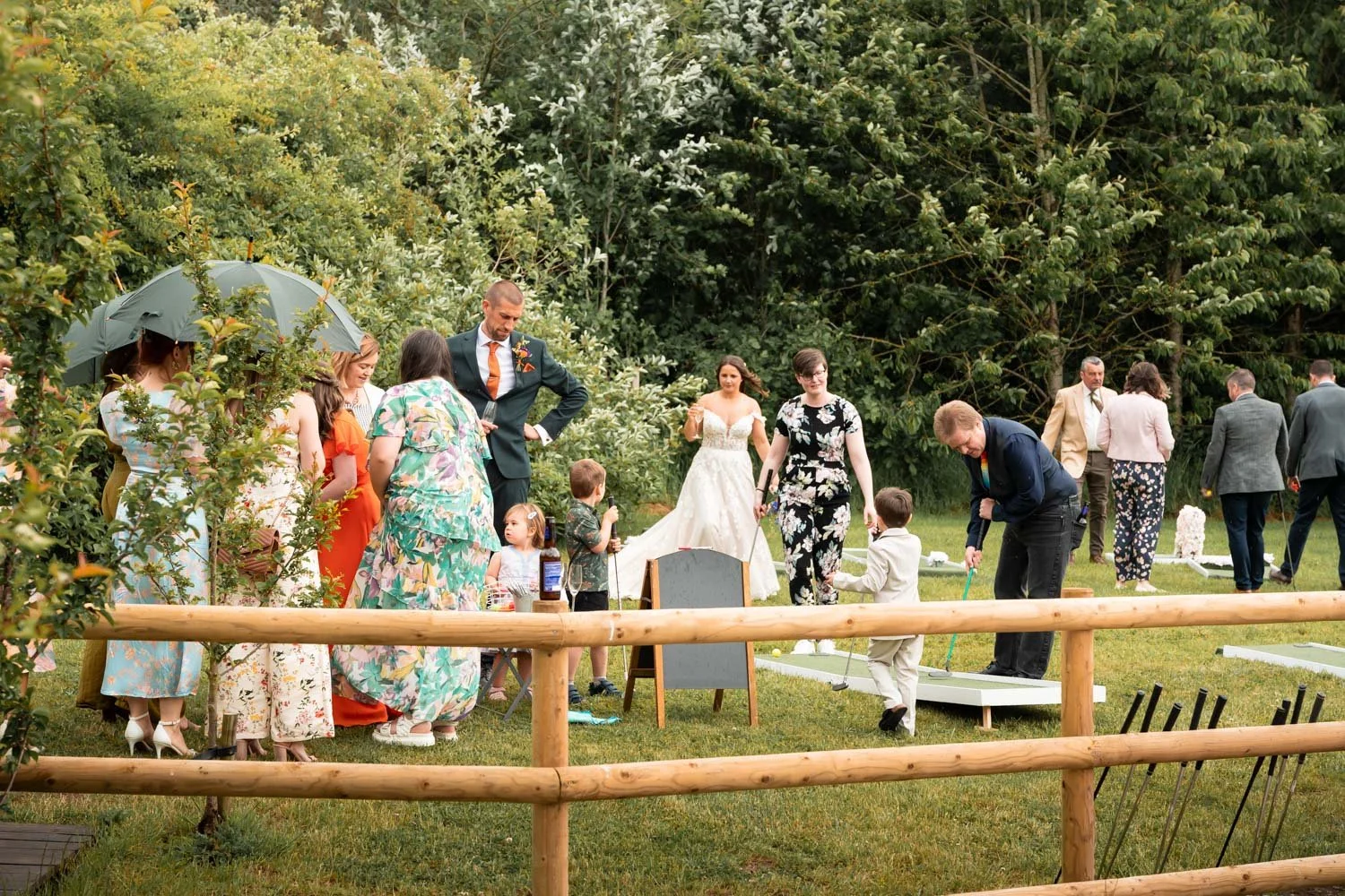 People gathered outdoors for a wedding celebration, with a bride in a white dress and guests in colorful attire playing mini golf.