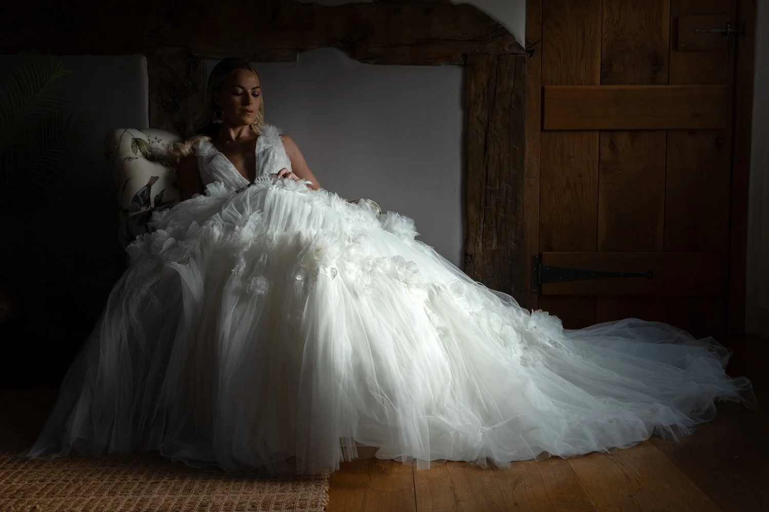 A woman in a white wedding dress sitting on a couch in a dimly lit room with wooden walls.