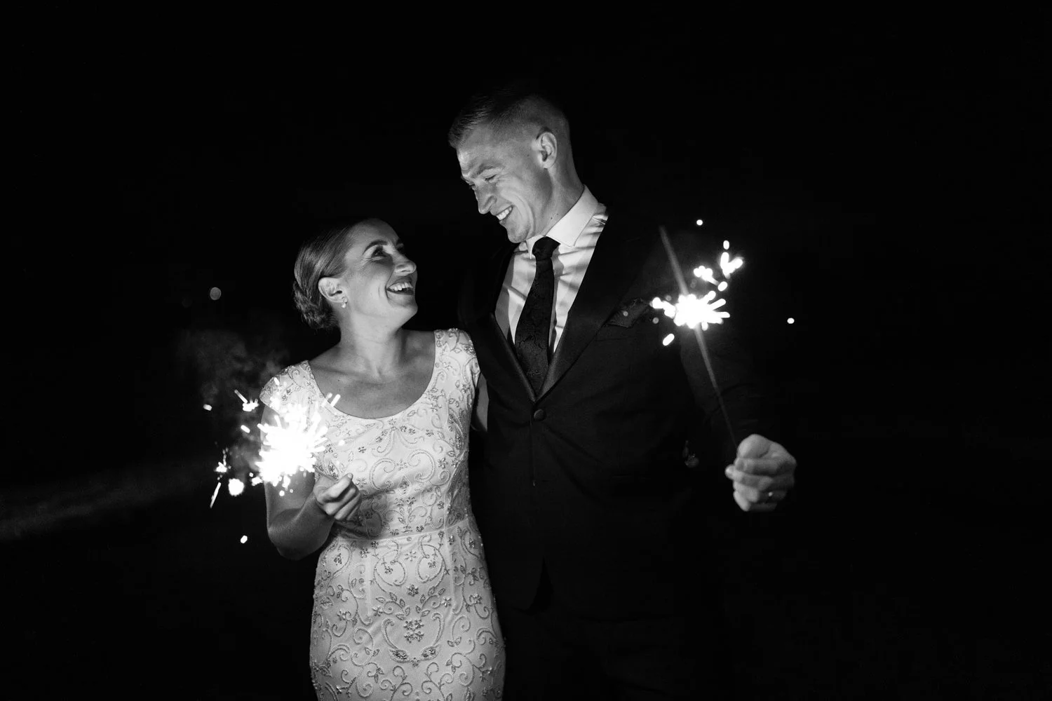 A happy couple holding sparklers at night, smiling at each other during a celebration.