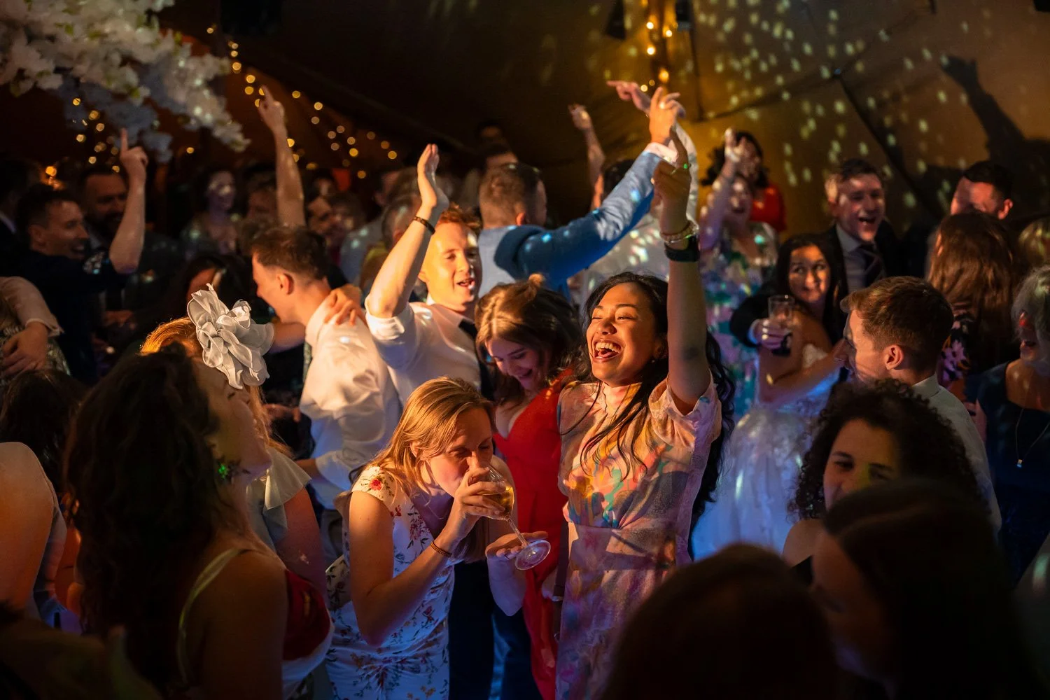 People dancing and celebrating at a lively party or wedding reception with colorful lighting and joyful expressions.