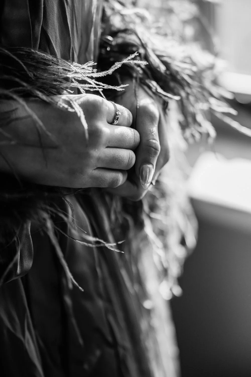 Black and white close-up of a person's hands holding a bundle of dried leaves or grasses, with the person wearing a ring and a textured jacket.