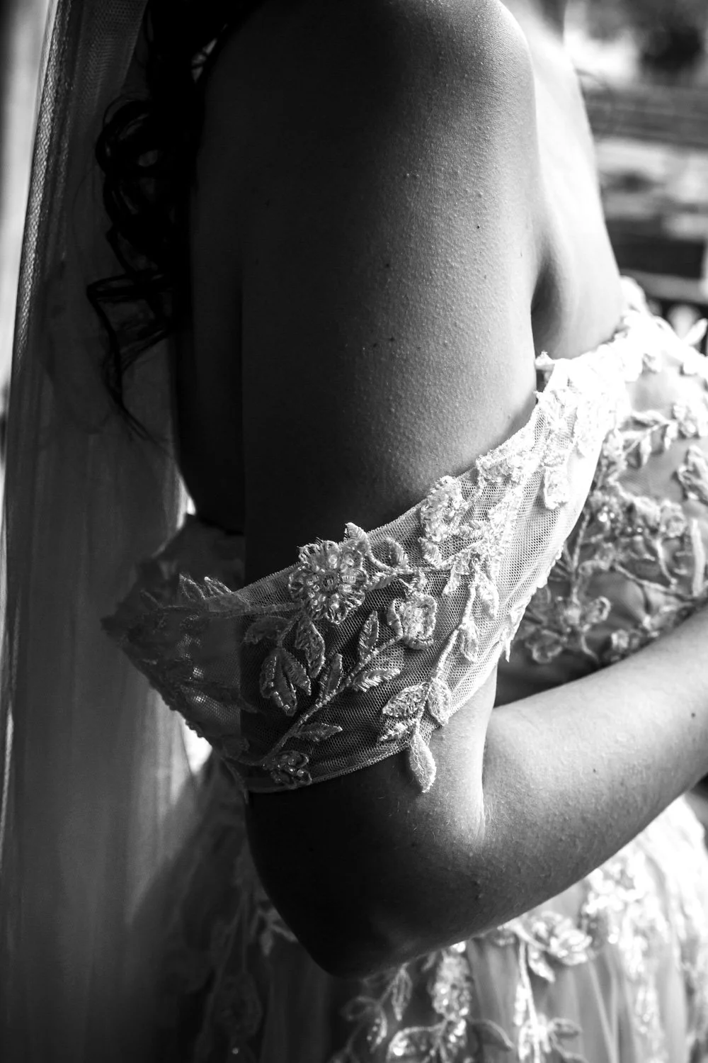 Close-up of a woman in a wedding dress with lace and floral embroidery, showing her shoulder and arm.